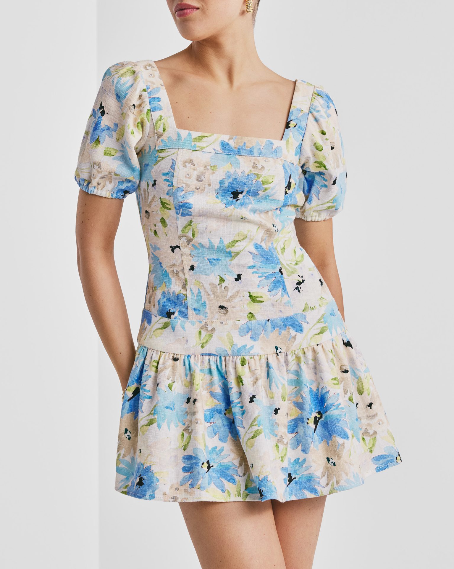 Woman in a short, blue, green, and beige floral dress with a square neck and puff sleeves.