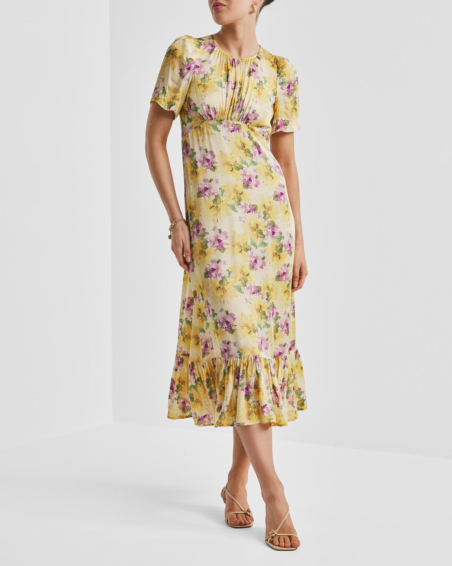 Yellow floral midi dress with short sleeves, ruffled hem, and nude sandals on a person.