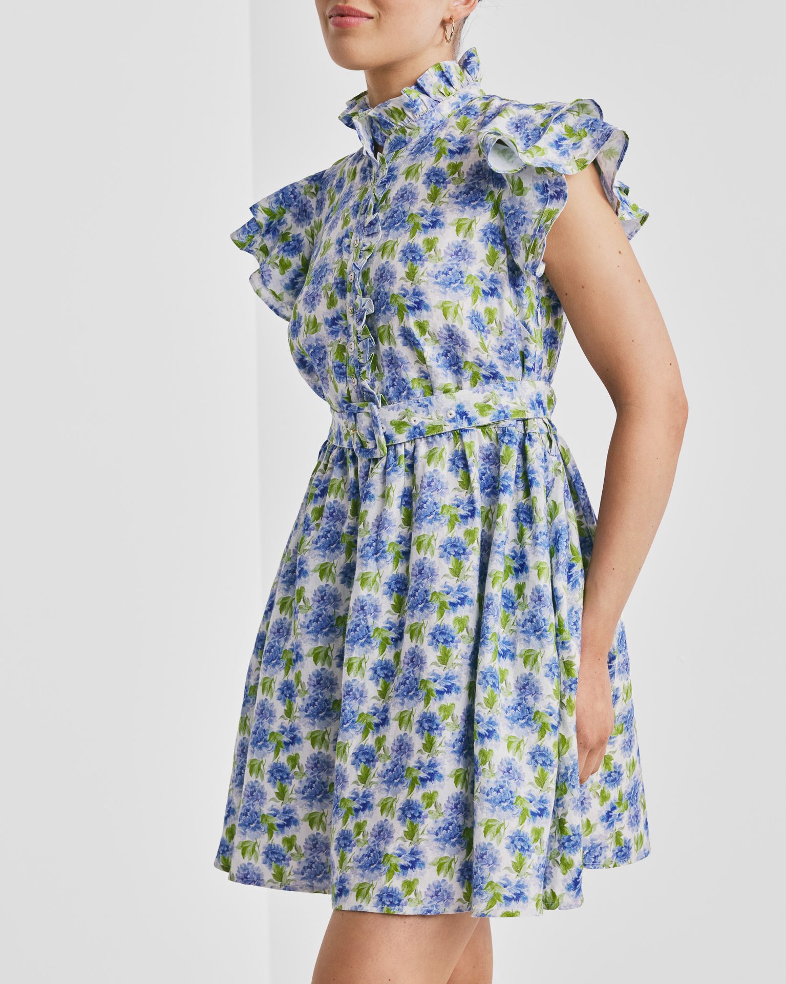 Woman in a white floral dress with blue flowers, ruffled high collar, cap sleeves, and a belt.