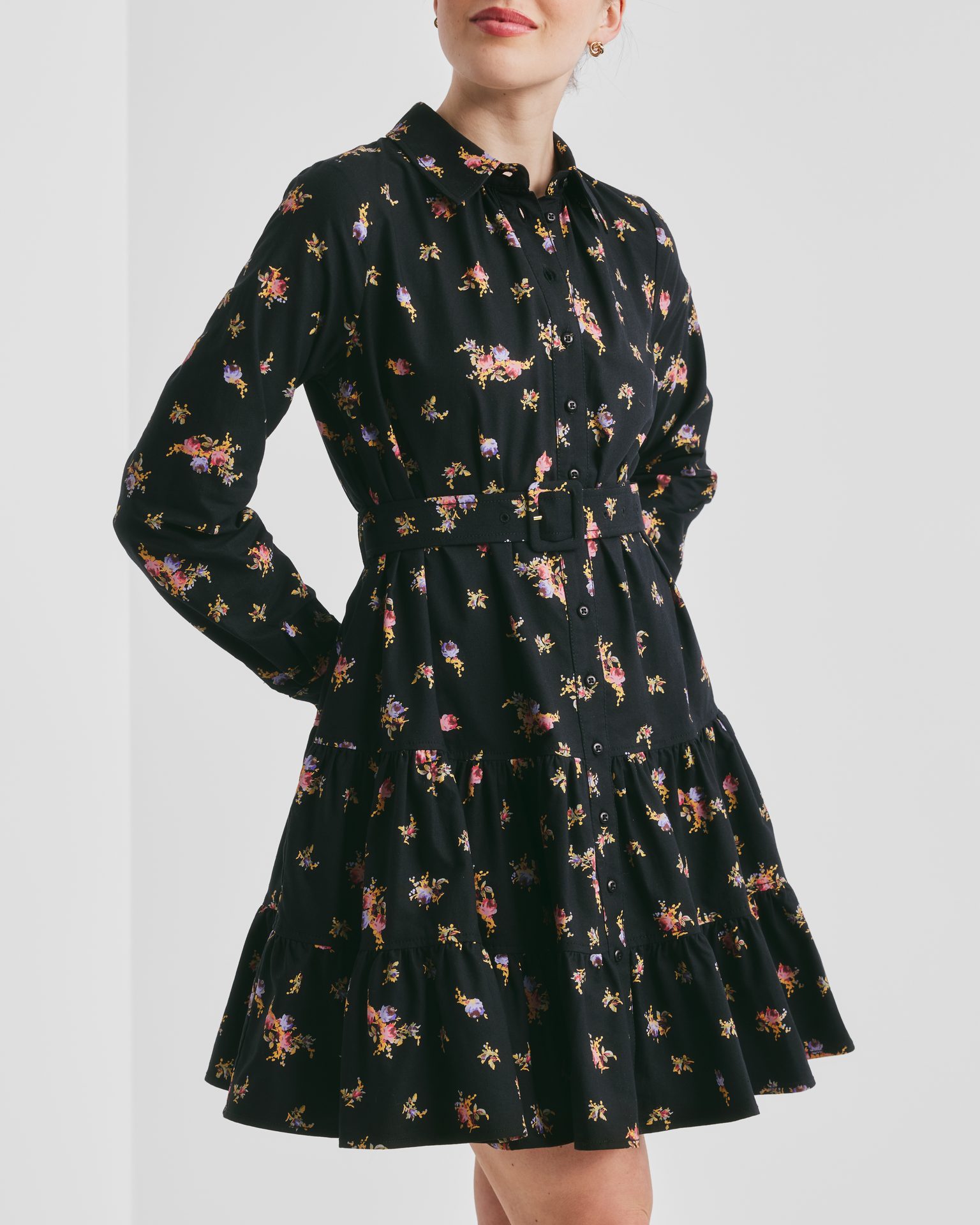 Woman in a black floral long-sleeve tiered dress with a belt.