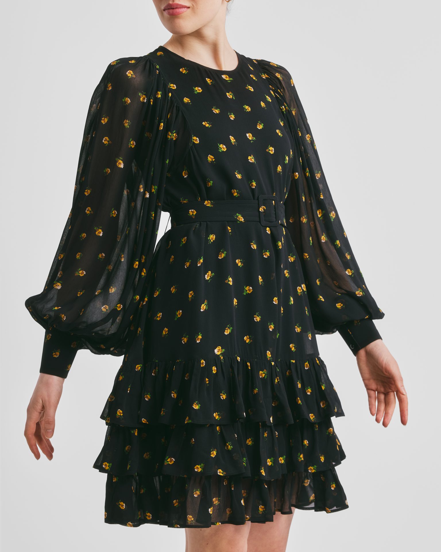 Woman in black mini dress with yellow floral print, puffy sleeves, belt, and tiered skirt.