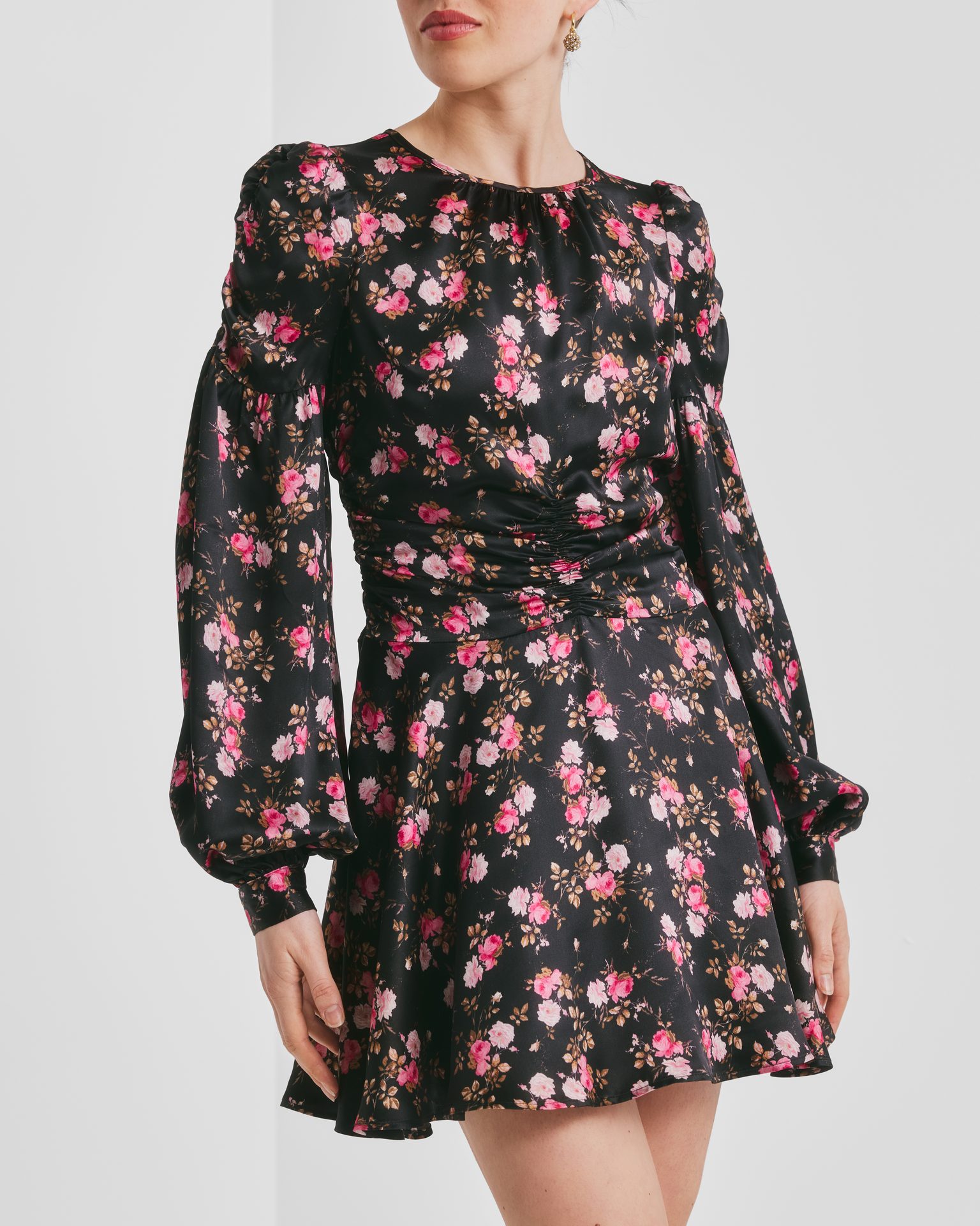 Woman in a black mini dress with pink rose print, long sleeves, and a ruched waist.