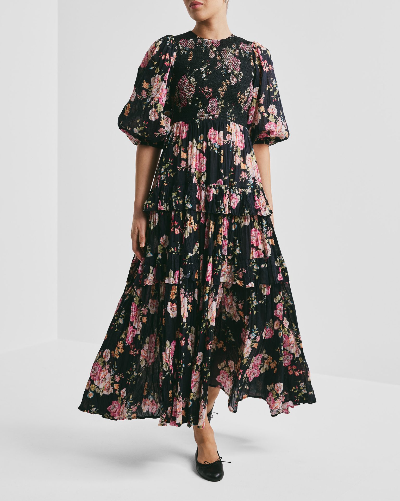Woman in a black floral tiered maxi dress with puffed sleeves.