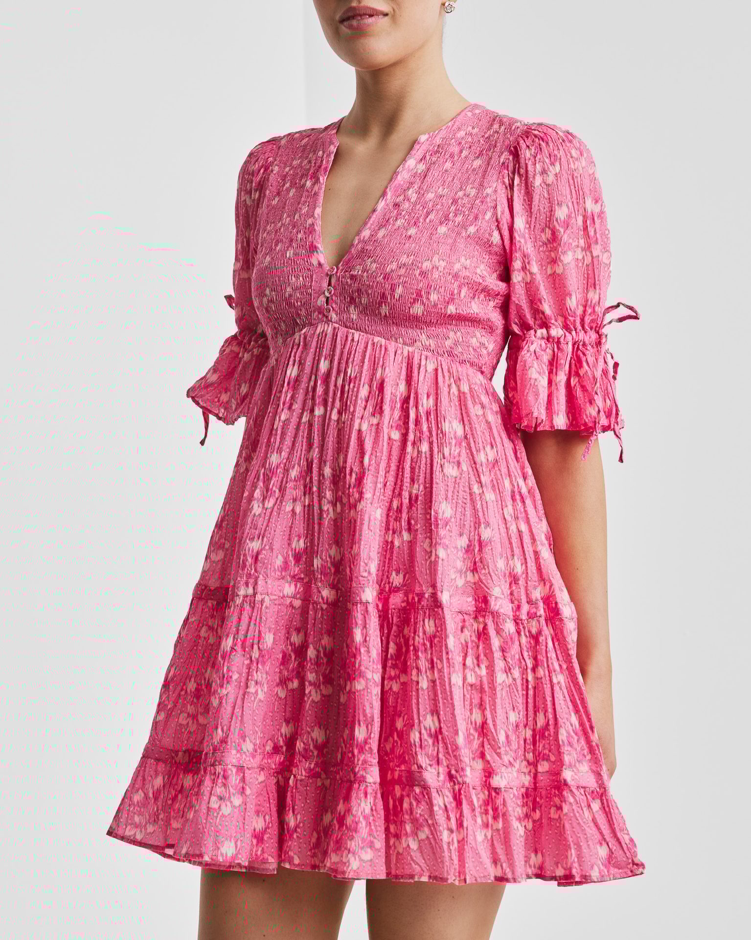Pink floral mini dress with V-neck, smocked bodice, puff sleeves, and tiered skirt.