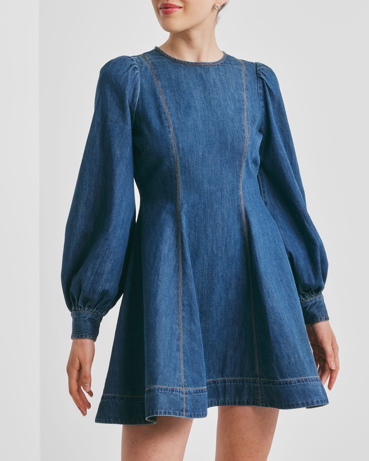 Woman in a long-sleeved denim mini dress with puffy sleeves and contrasting stitching.