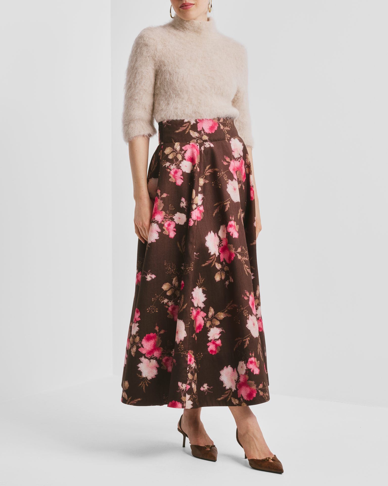 Model wears a beige fuzzy sweater, brown floral skirt with pink flowers, and brown heels.