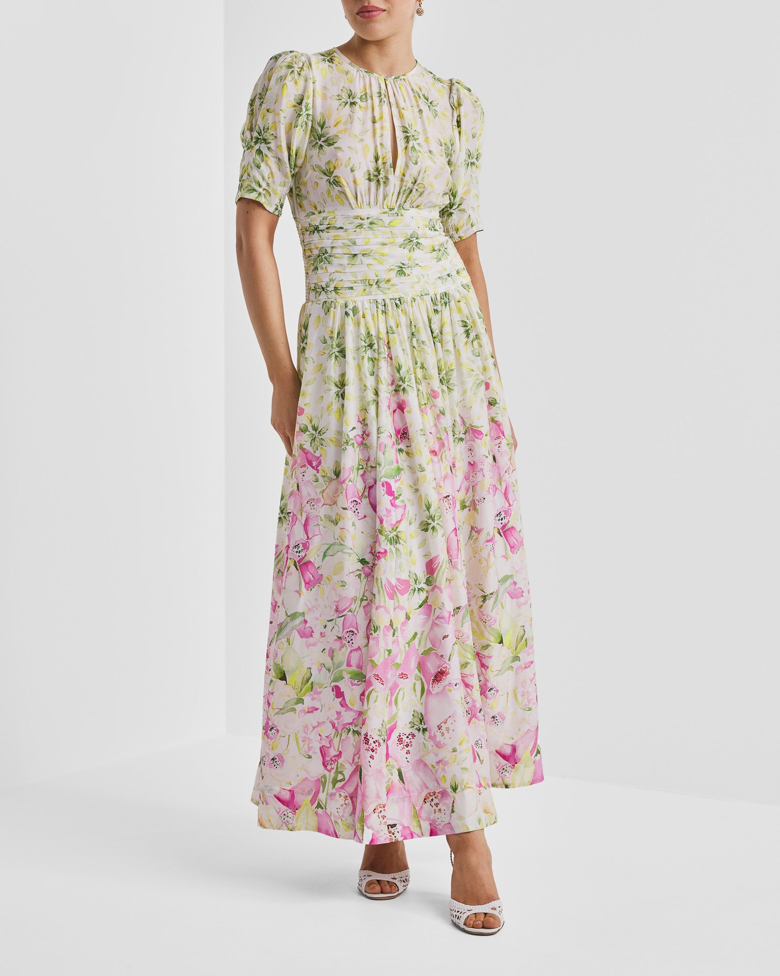 Woman in a white maxi dress with green and pink floral print, puff sleeves, and cinched waist.