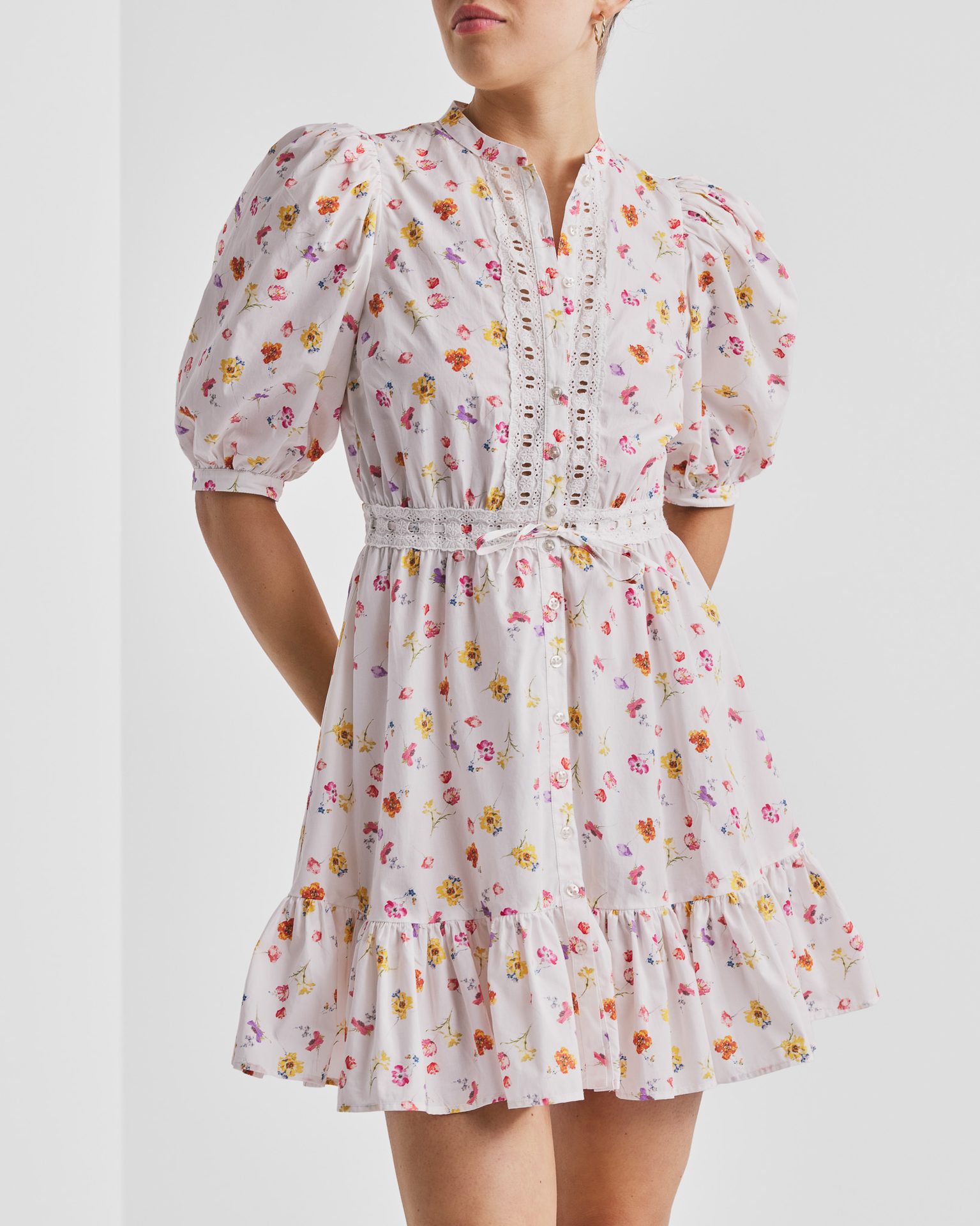 White floral mini dress with puff sleeves, lace trim, and a tied waist.