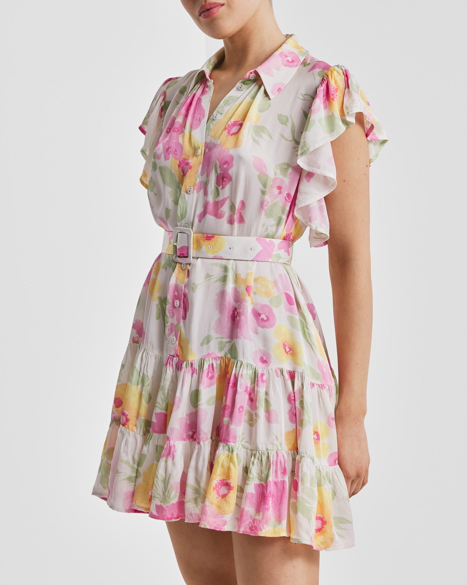 Woman in a white floral mini dress with ruffled sleeves and a white belt.
