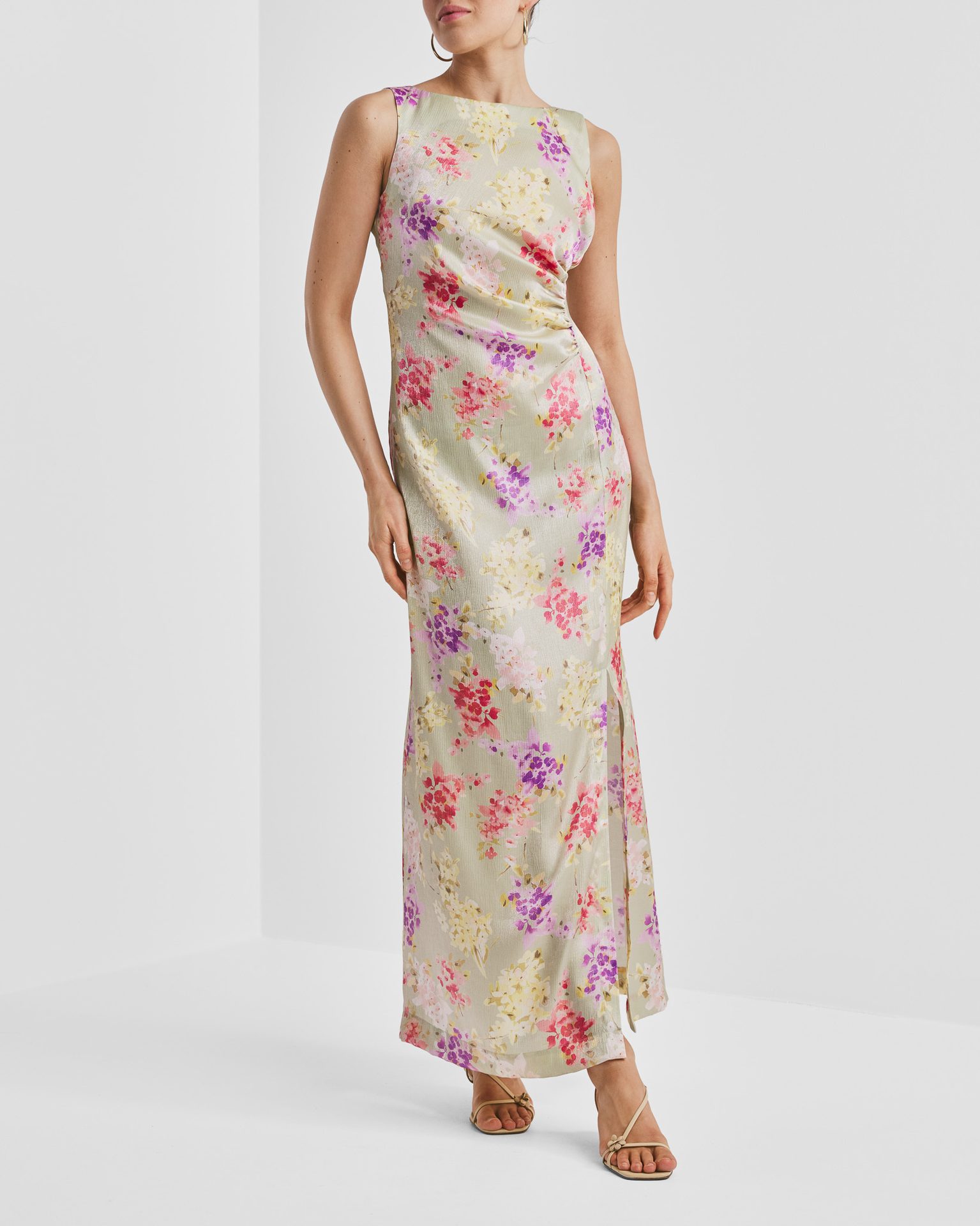 A woman wears a sleeveless light green floral maxi dress with a side slit and nude sandals.