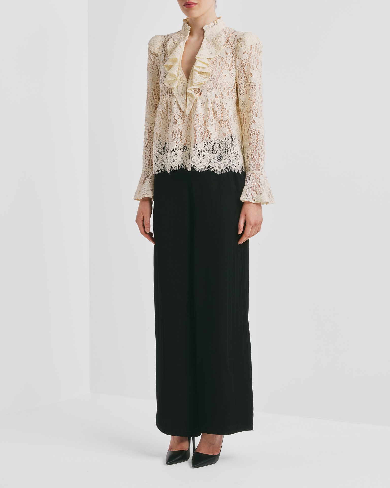 A person in a cream ruffled lace blouse and black wide-leg pants with black heels.