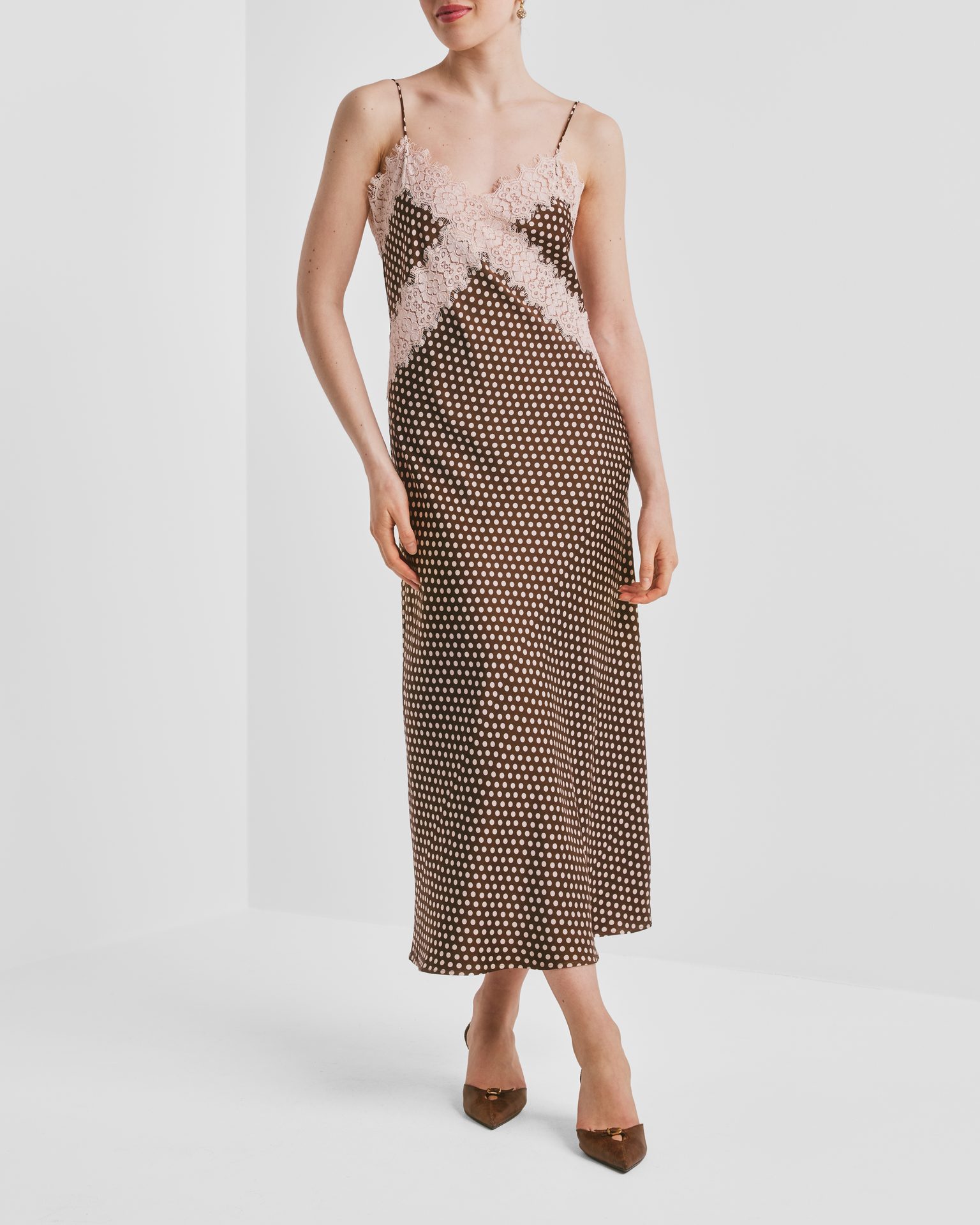 Woman in brown polka dot slip dress with pink lace trim, wearing brown heels.