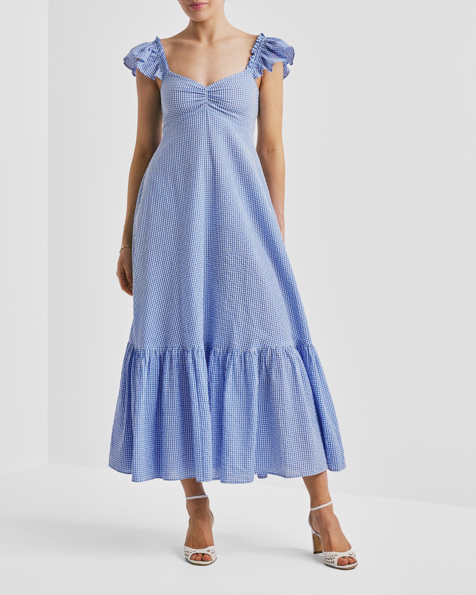 Woman in a blue and white gingham midi dress with ruffled sleeves and white high heels.