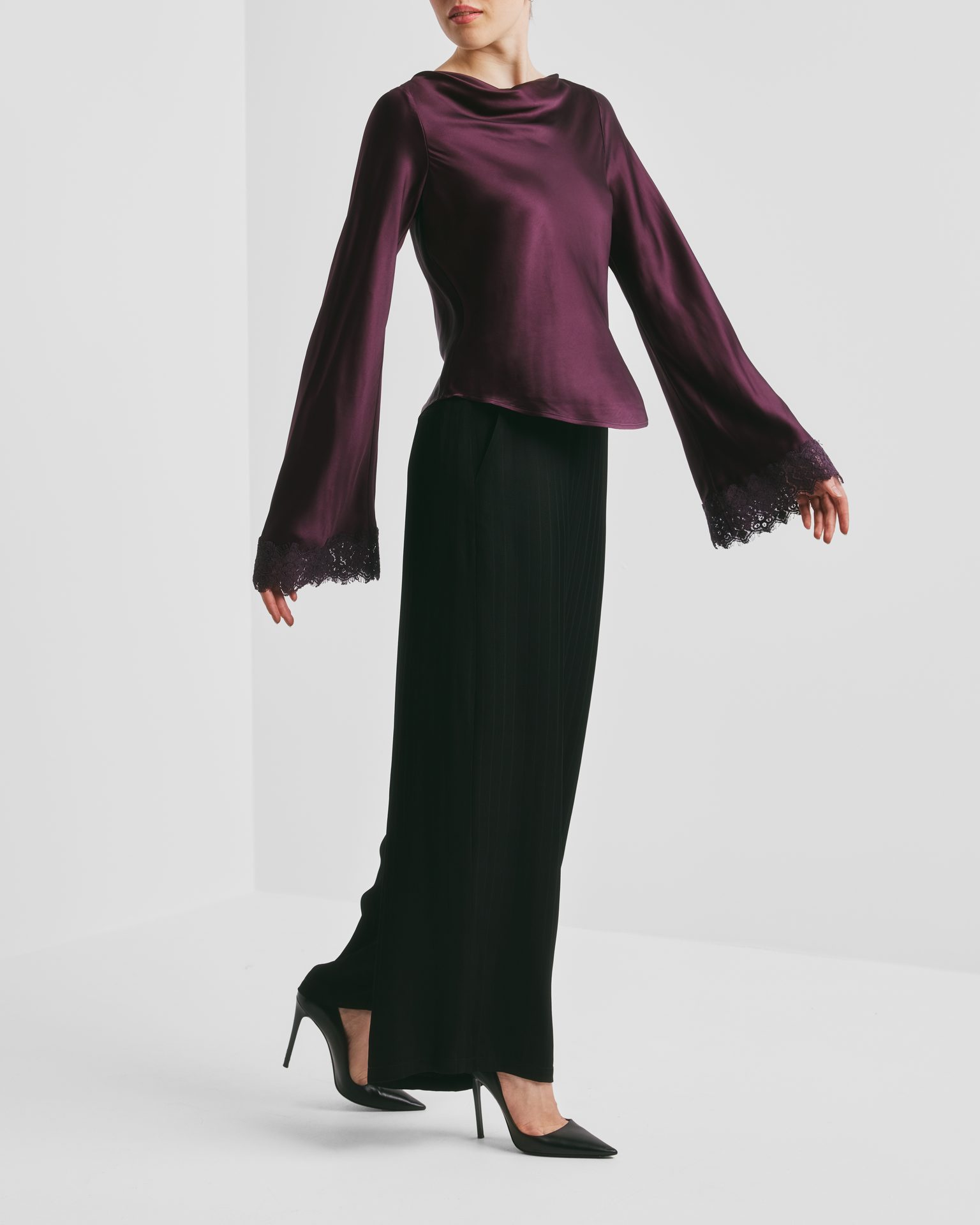 Person in plum satin cowl neck blouse with lace bell sleeves, black wide-leg pants, and heels.