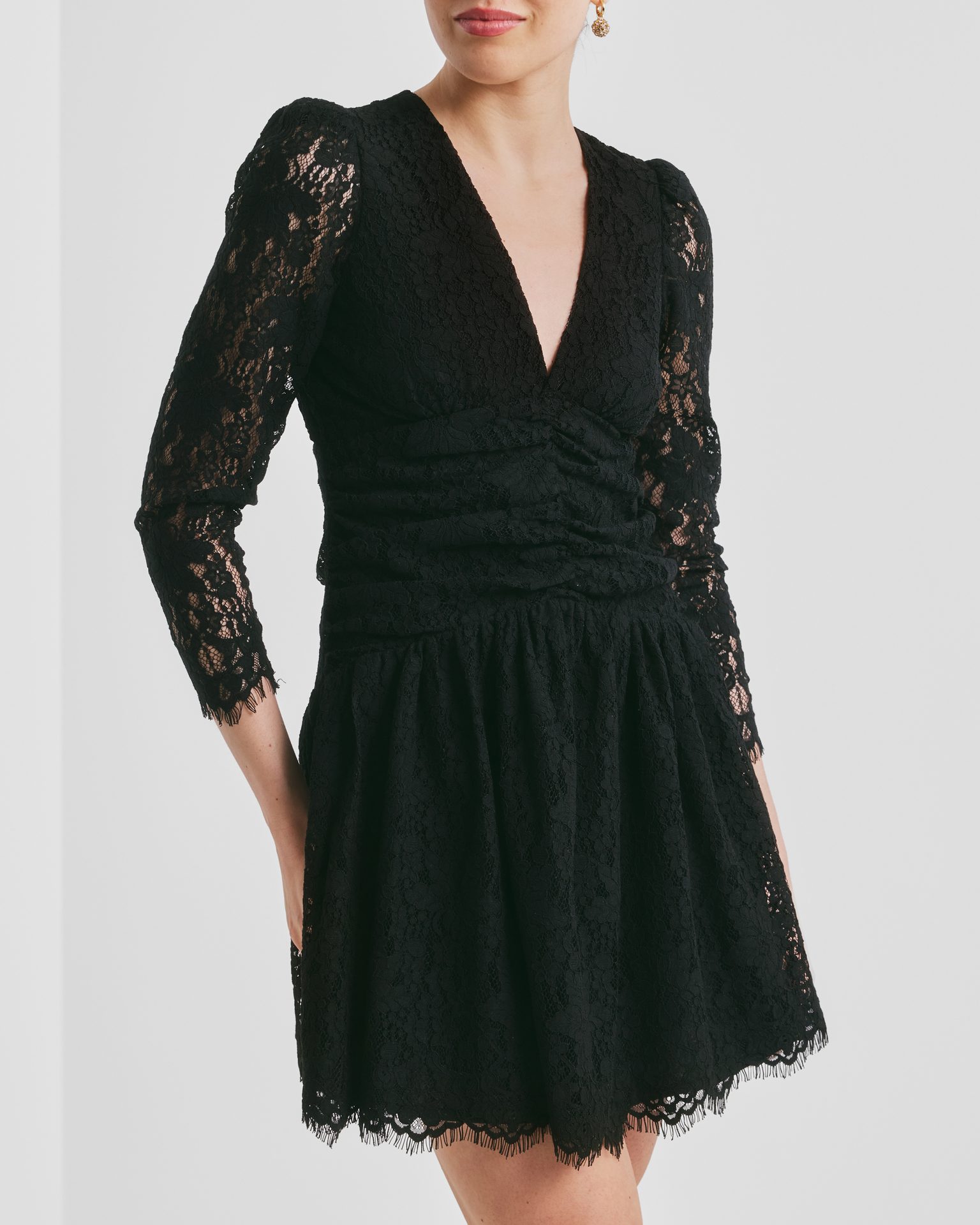 A black lace V-neck mini dress with a ruched bodice, 3/4 sleeves, and scalloped hem.