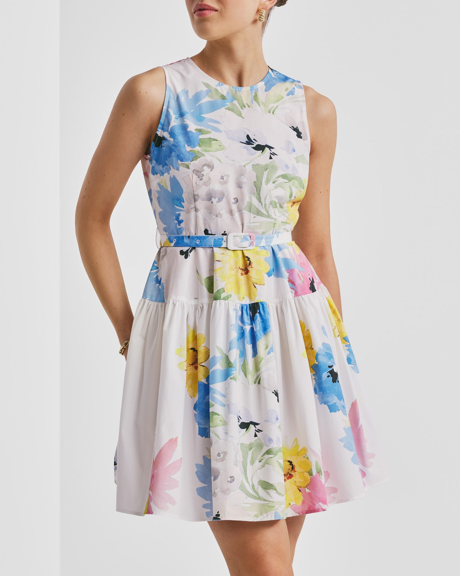 Woman in sleeveless white floral dress with blue belt and tiered skirt.