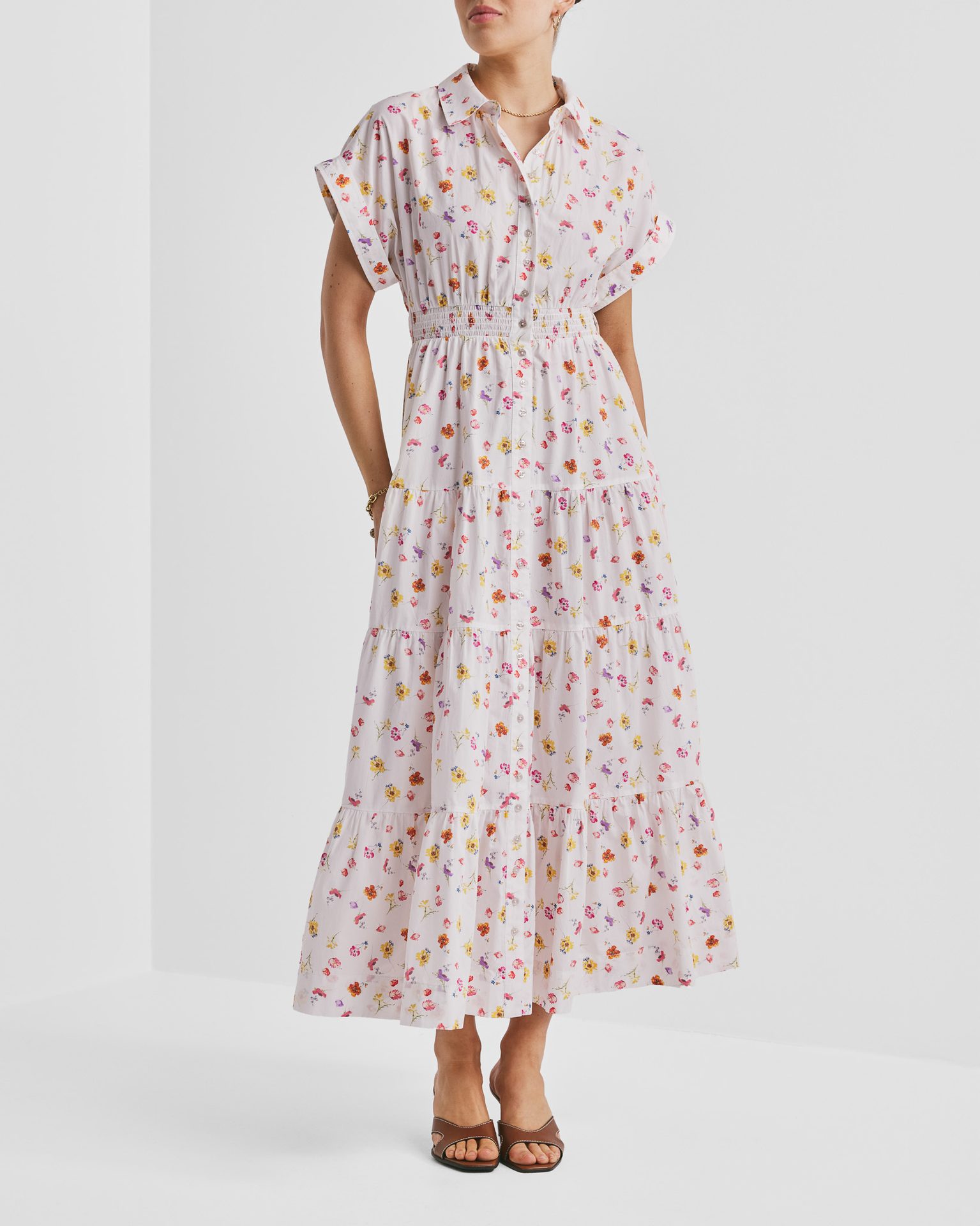 Woman in a white collared, short-sleeve, tiered floral midi dress and brown sandals.