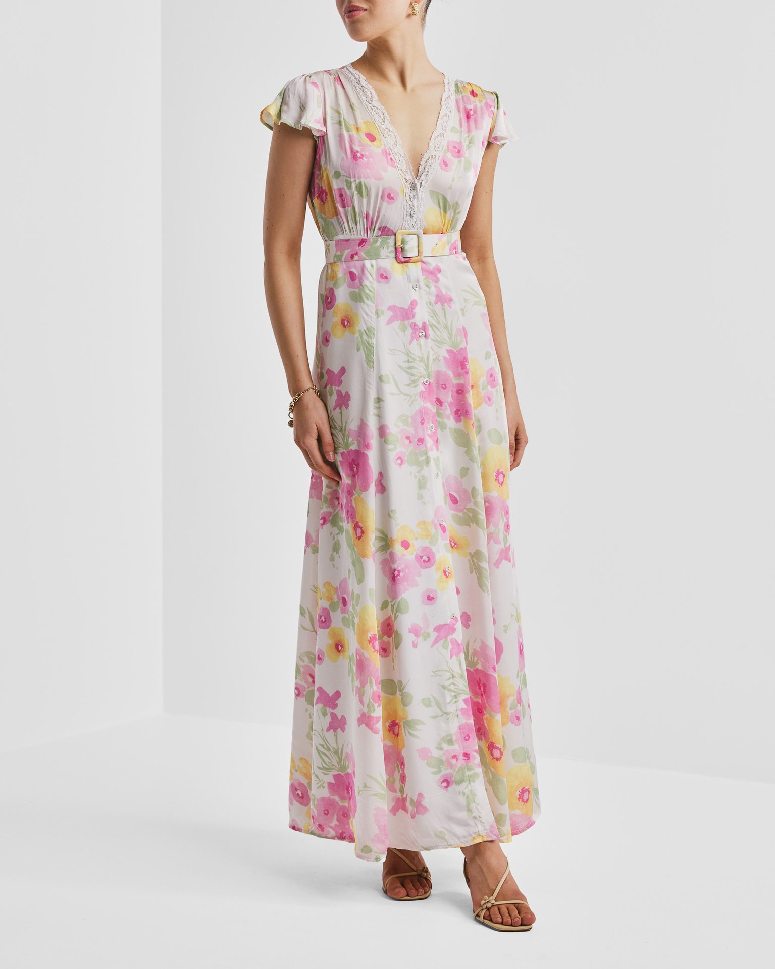 A woman in a floral maxi dress with pink and yellow flowers, a V-neck, short sleeves, and a pink belt.