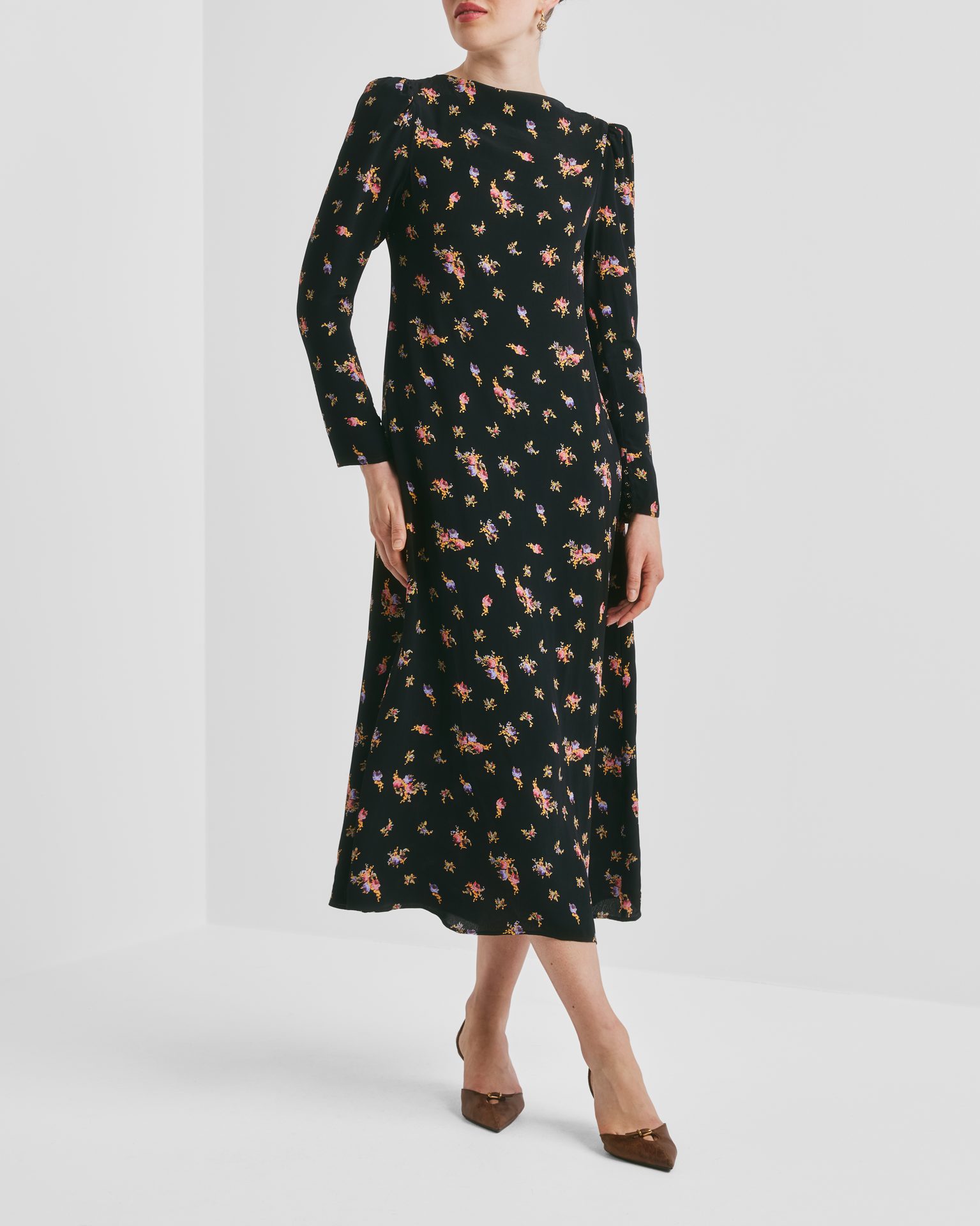 A woman in a black long-sleeved floral midi dress with pink, yellow, and purple flowers, and brown heels.