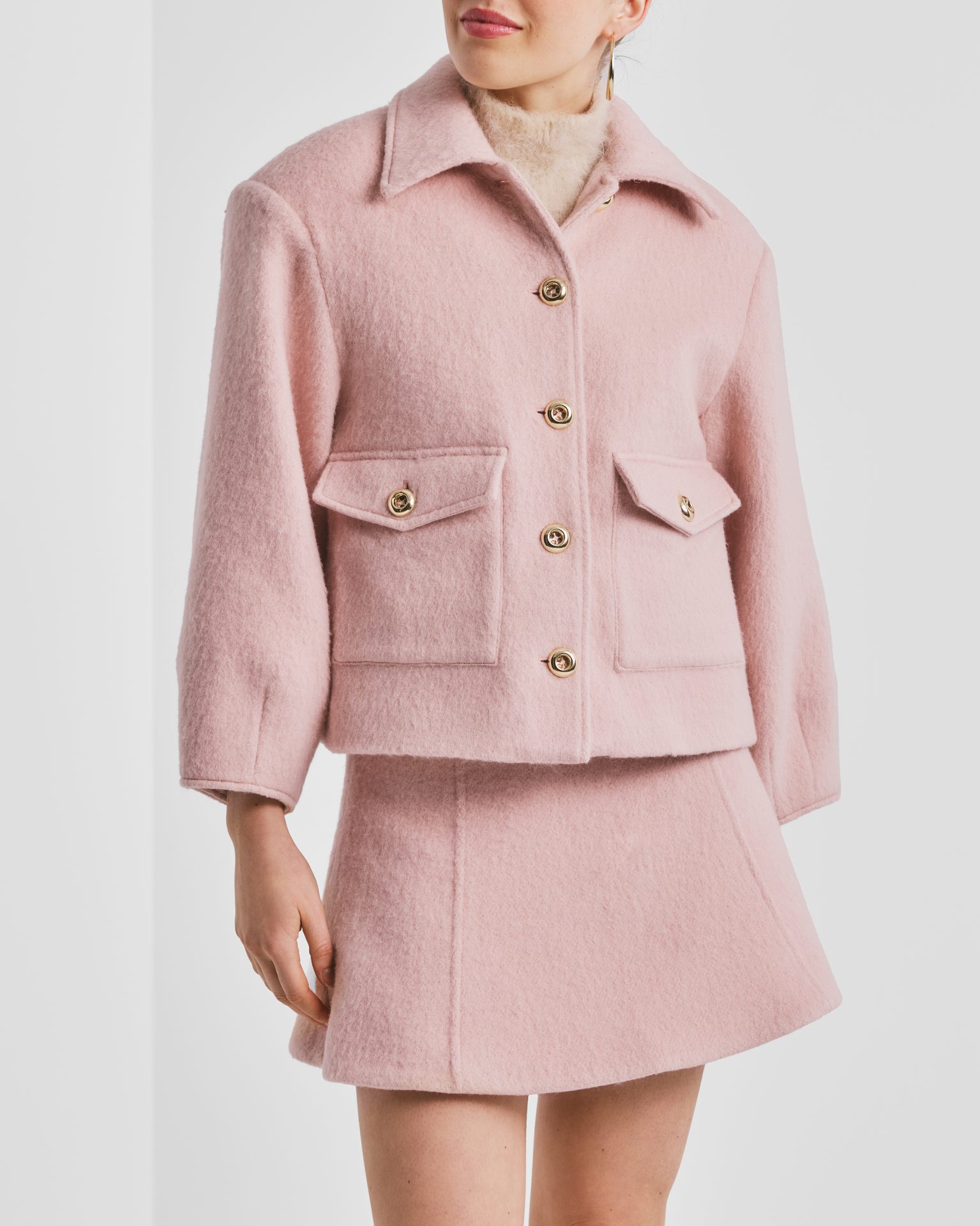 Woman in a pink wool jacket with gold buttons and matching mini skirt.