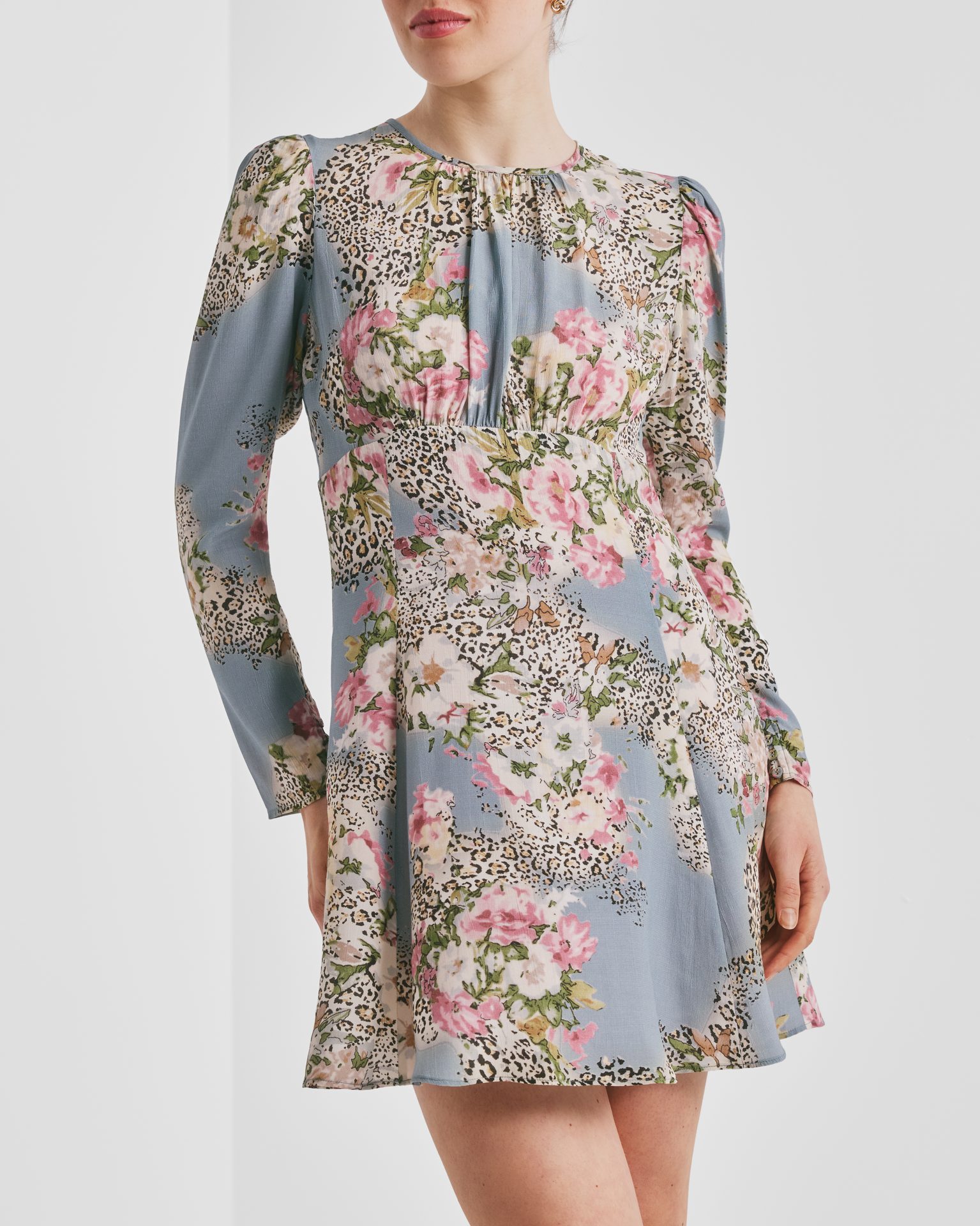 A woman wears a light blue floral and leopard print mini dress with long sleeves.