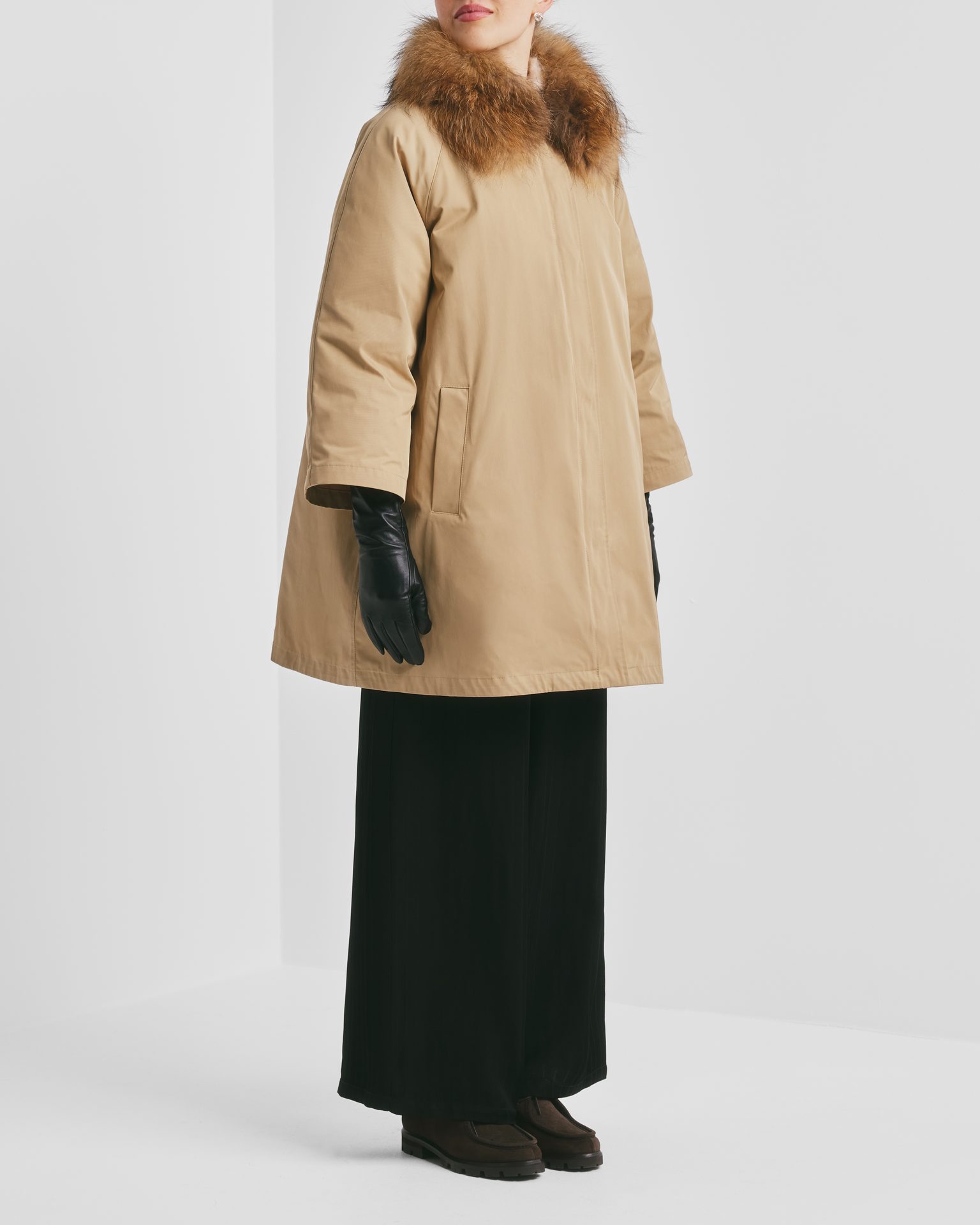 A person wears a beige fur-collar parka, black gloves, wide-leg pants, and brown shoes.