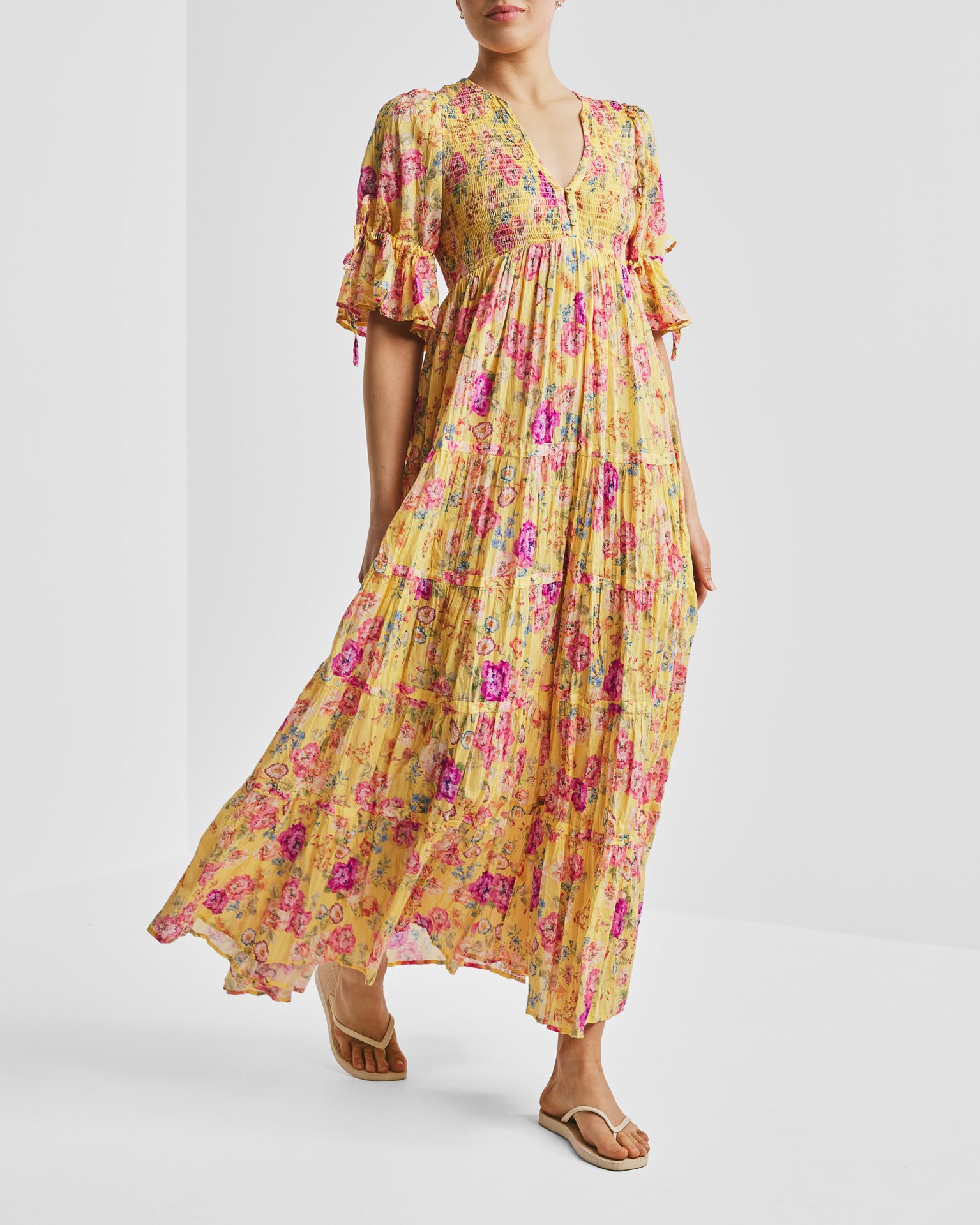 Woman in a vibrant yellow floral maxi dress with smocked top and tiered skirt.