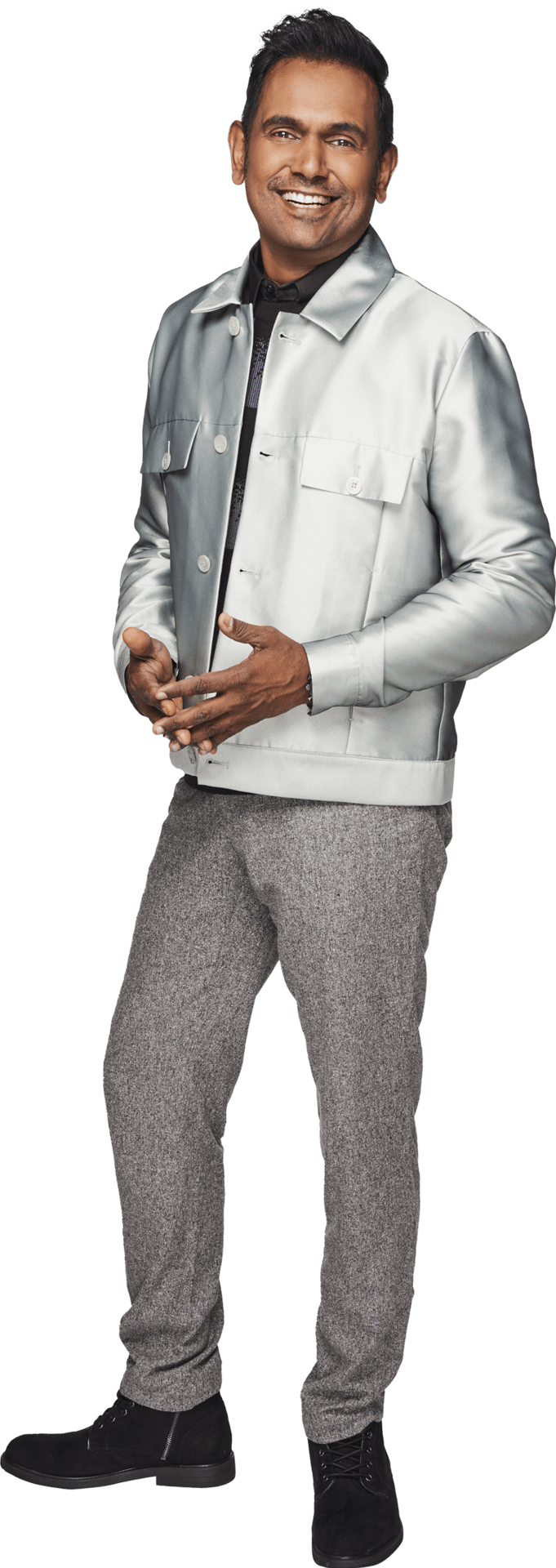 Smiling man in a silver jacket and gray pants, standing with hands clasped.