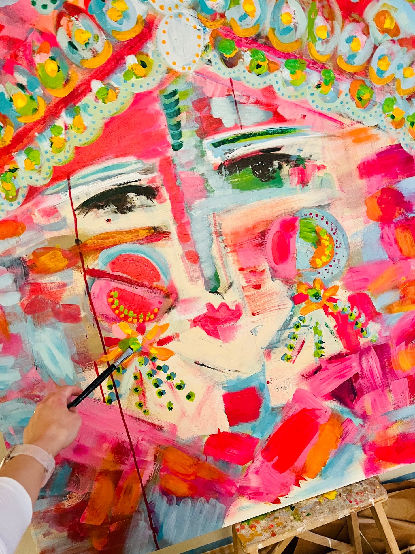 Hand painting a vibrant, abstract, colorful portrait on an easel.