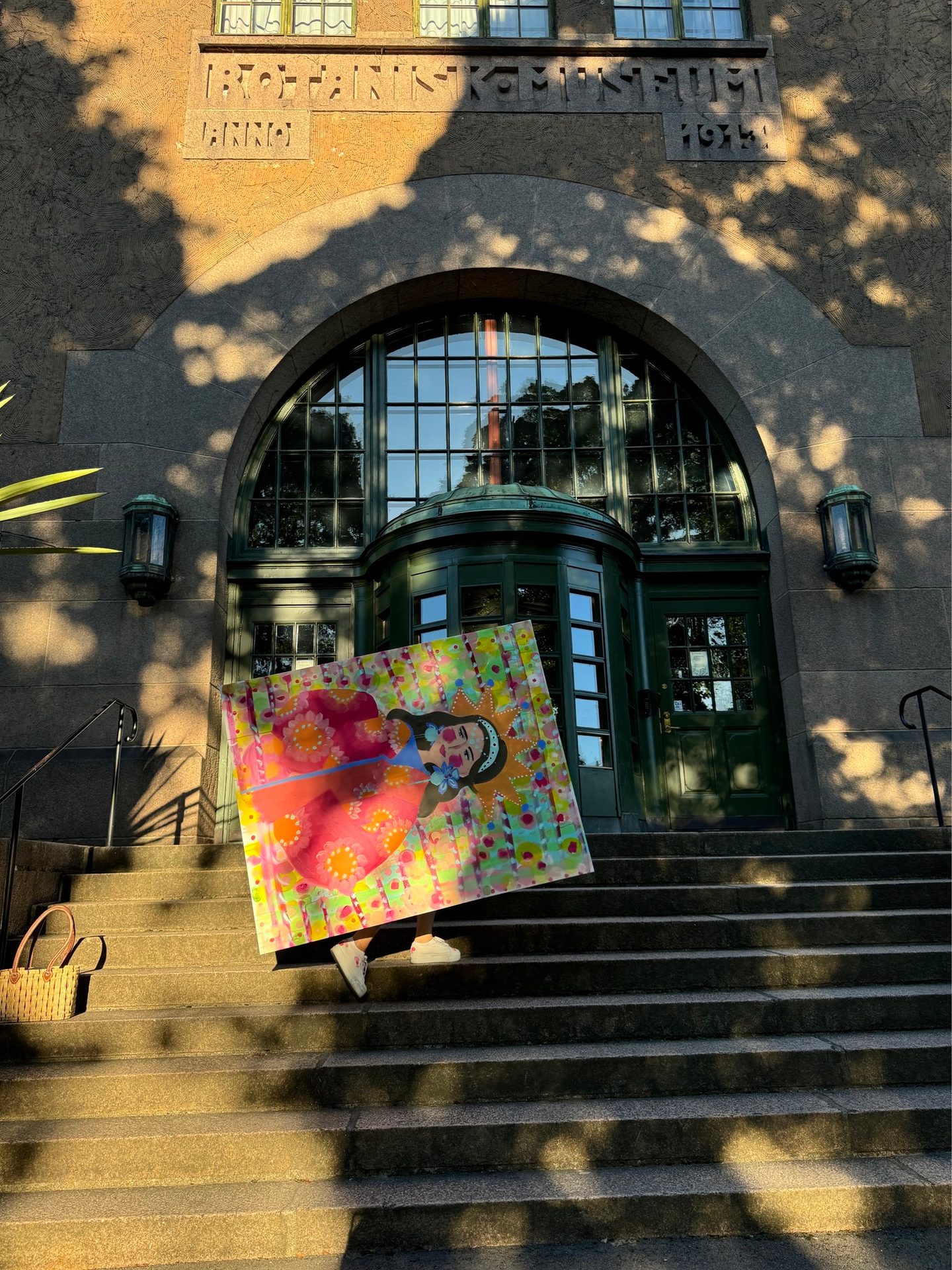 Colorful painting carried up sunlit stairs towards a grand arched building entrance.