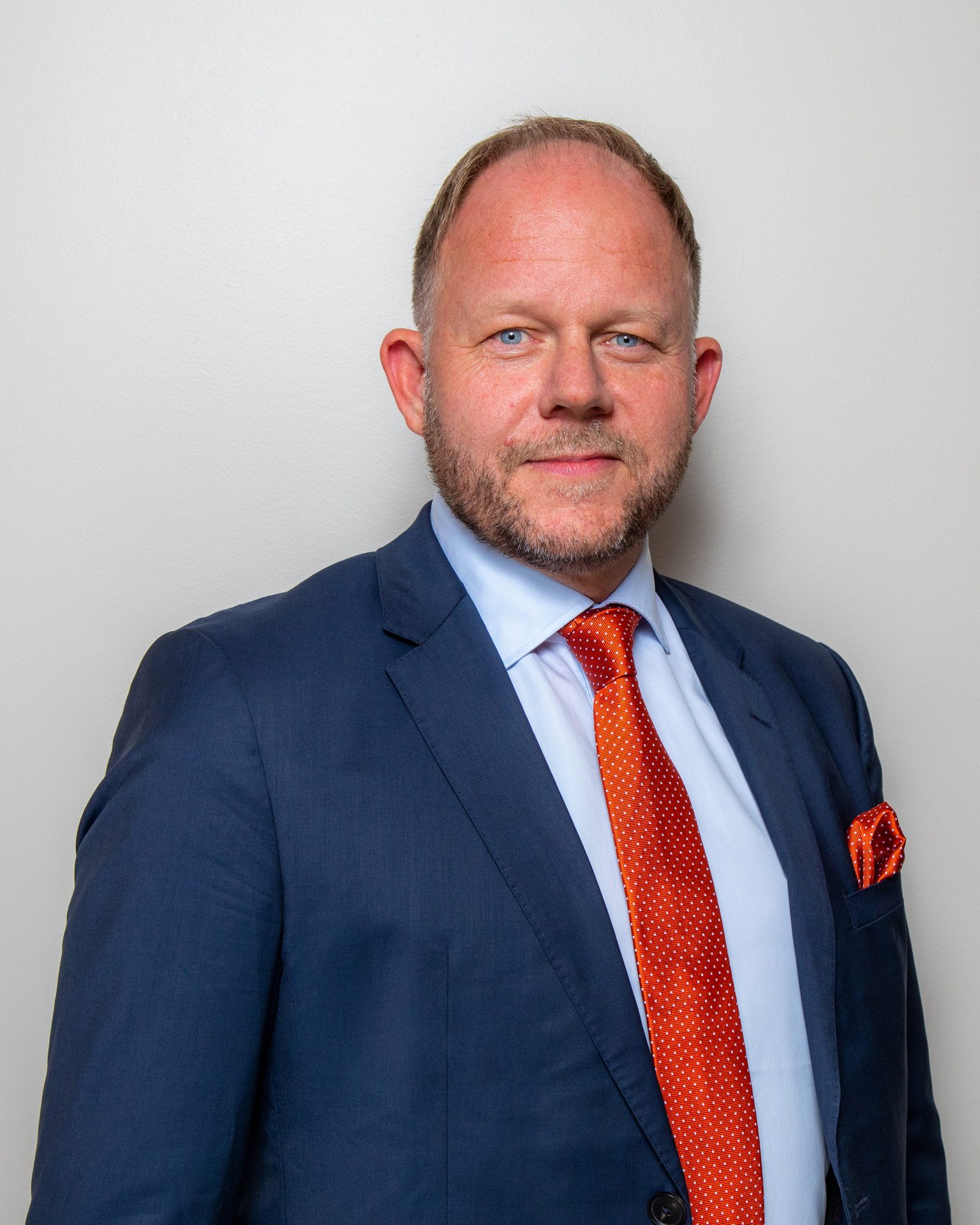 Portrait of a man in a blue suit with an orange tie and pocket square.