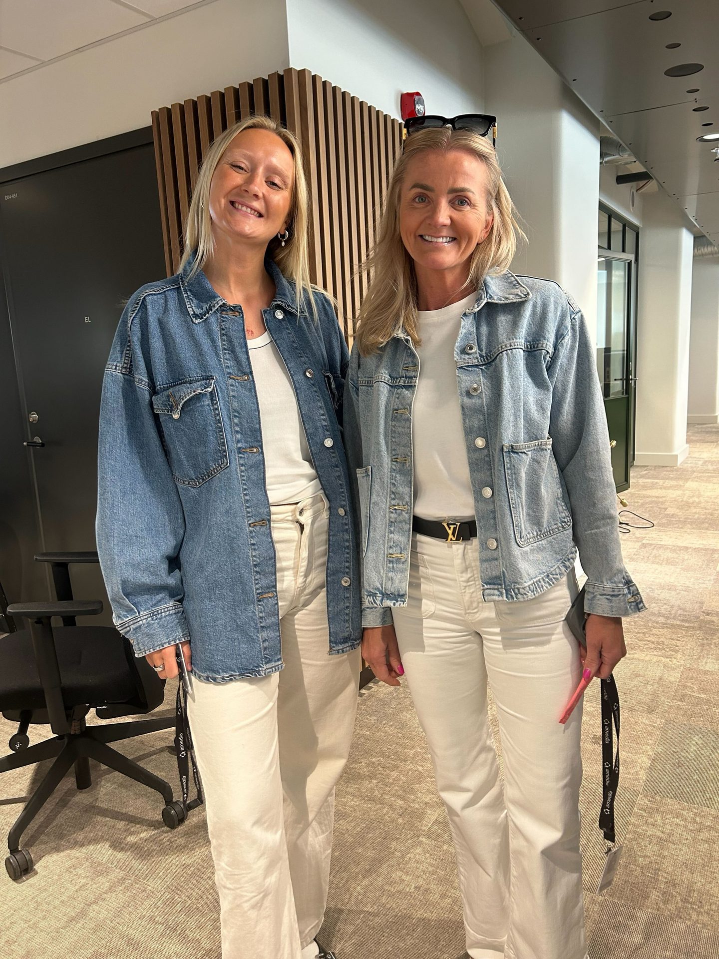 Two smiling women in denim jackets, white t-shirts, and white pants.