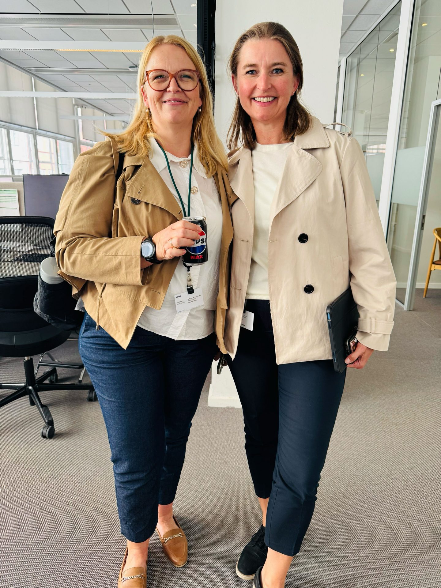 Two women smiling in an office. One holds a Pepsi, the other a tablet.