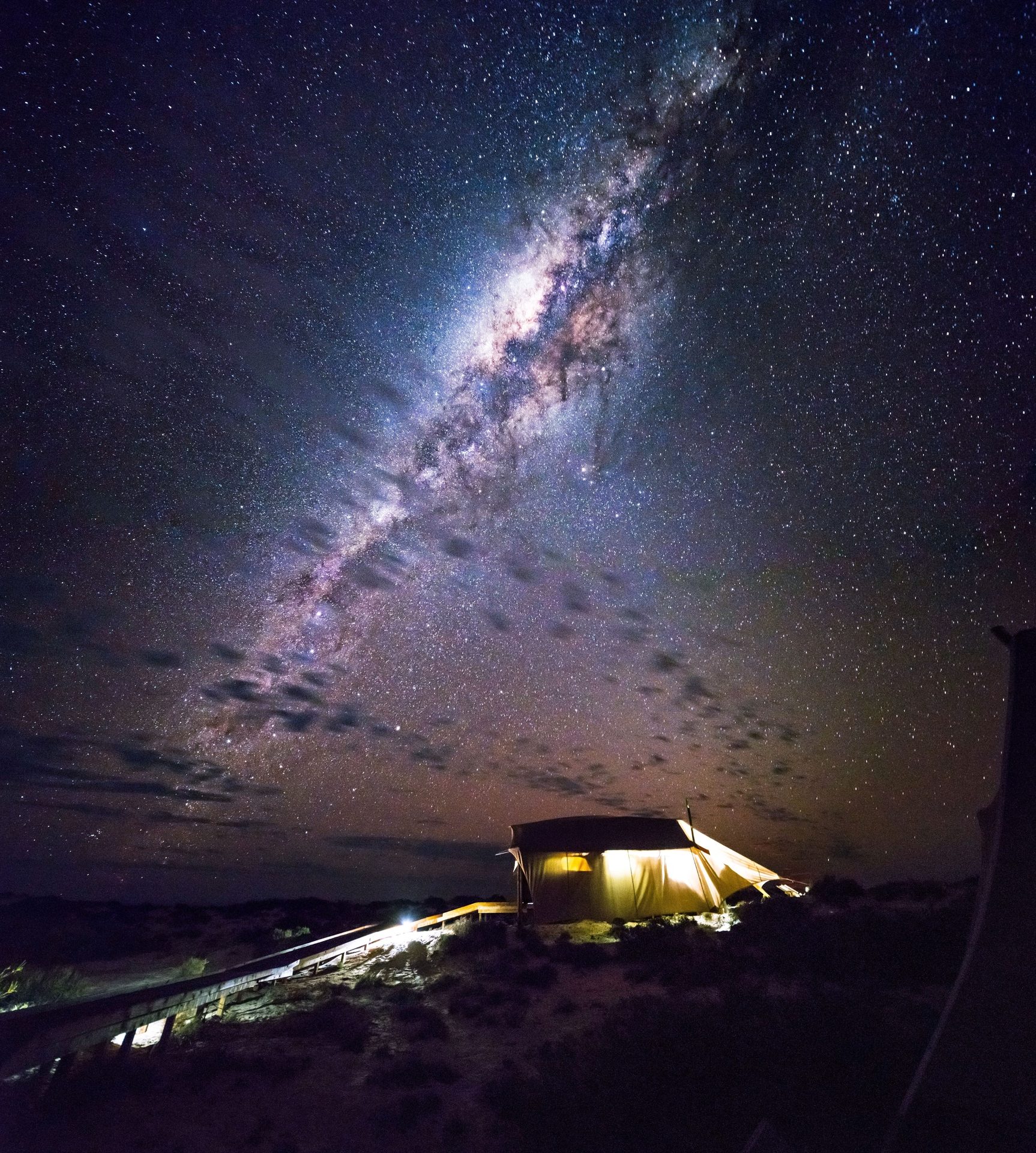 Milky Way illuminates a tent and a pathway in a dark, starry night landscape.