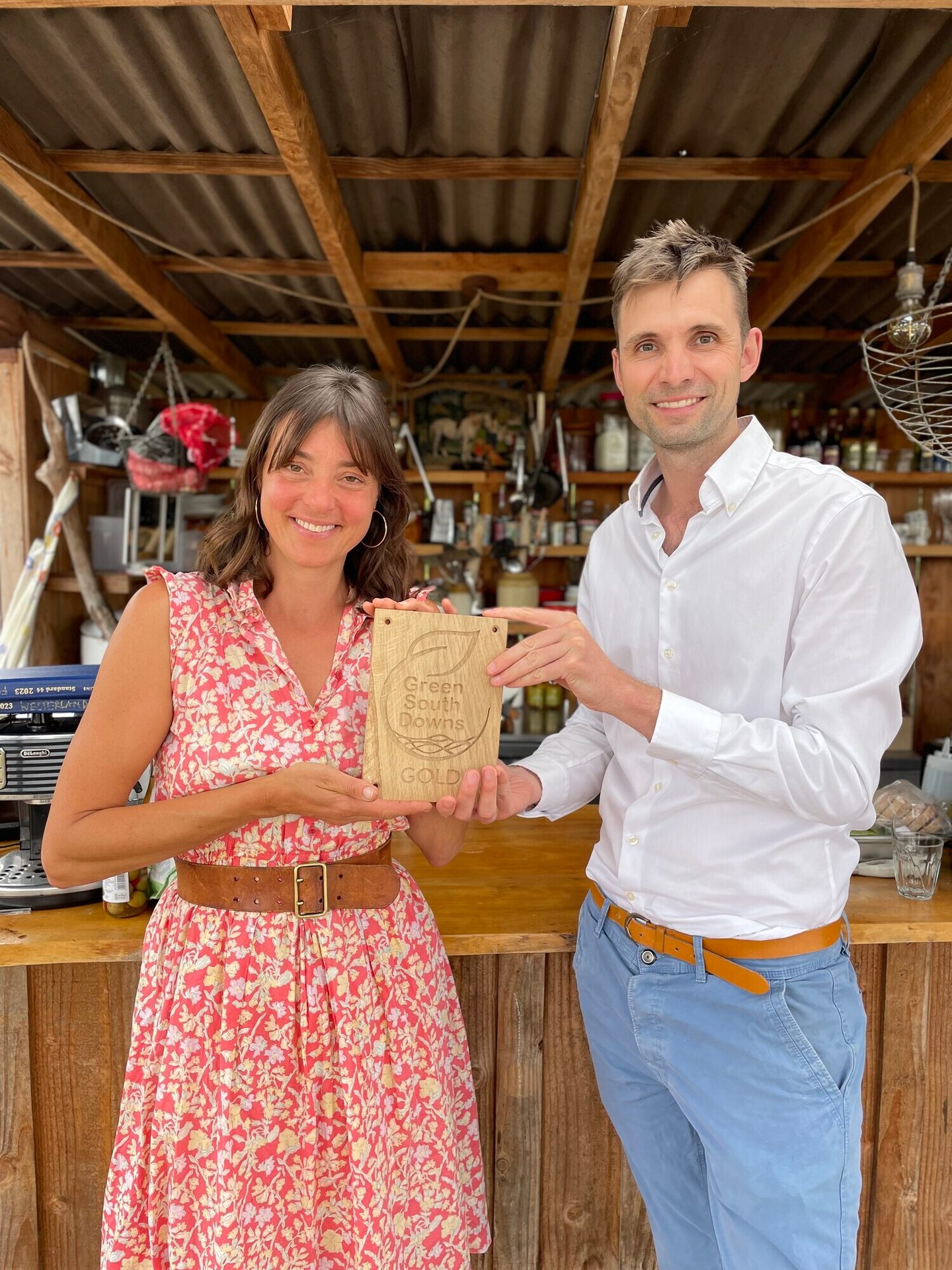 Smiling man and woman hold a "Green South Downs GOLD" wooden plaque.