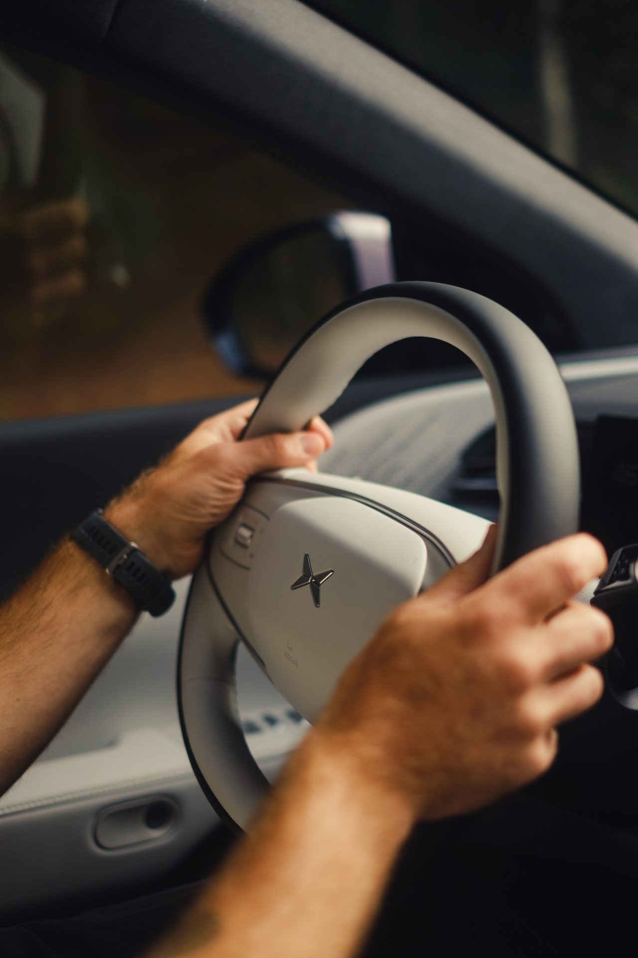 Hands on a Polestar steering wheel, with a smartwatch visible.