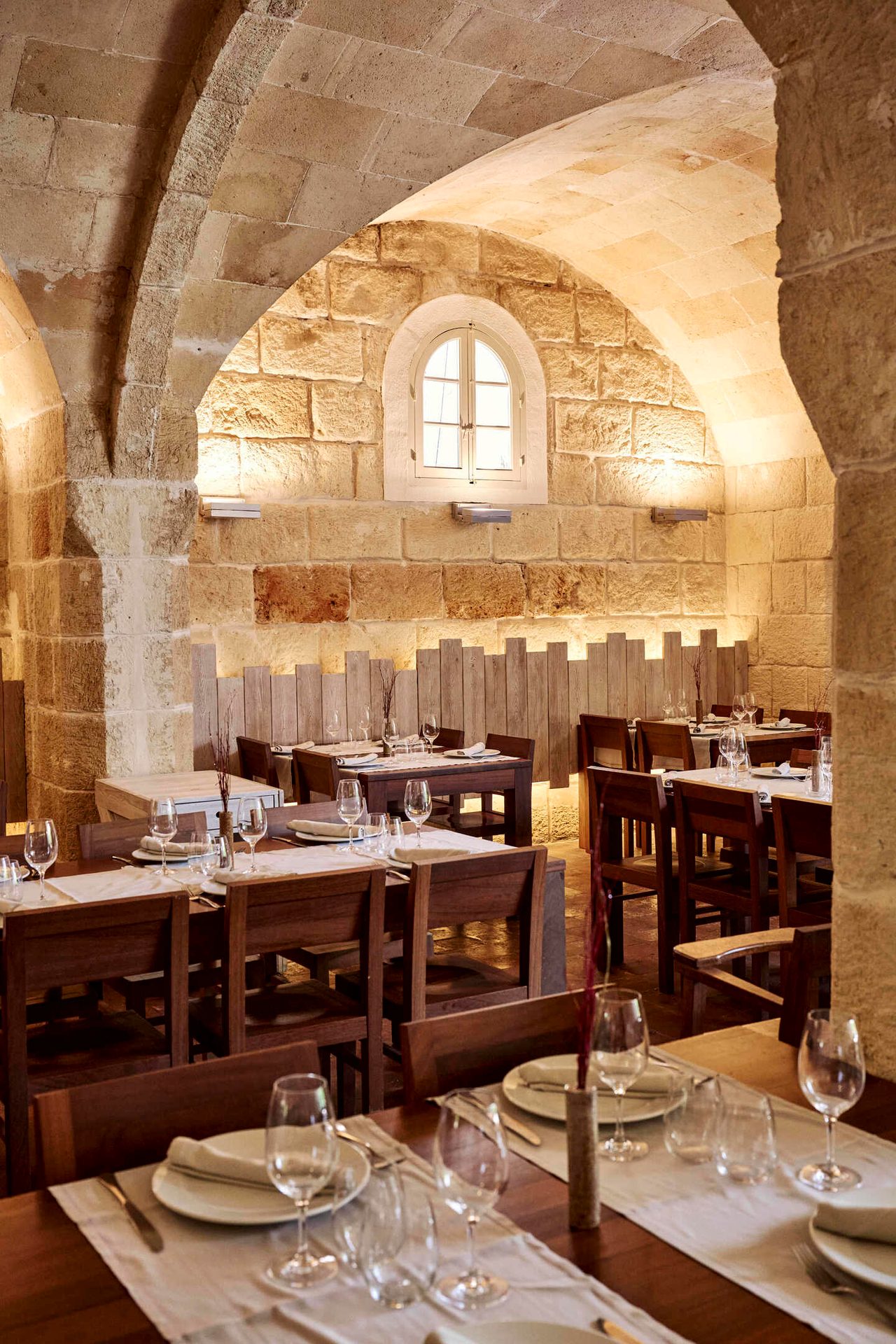 Inside a stone-walled restaurant with arched ceilings, set tables, and wooden chairs.