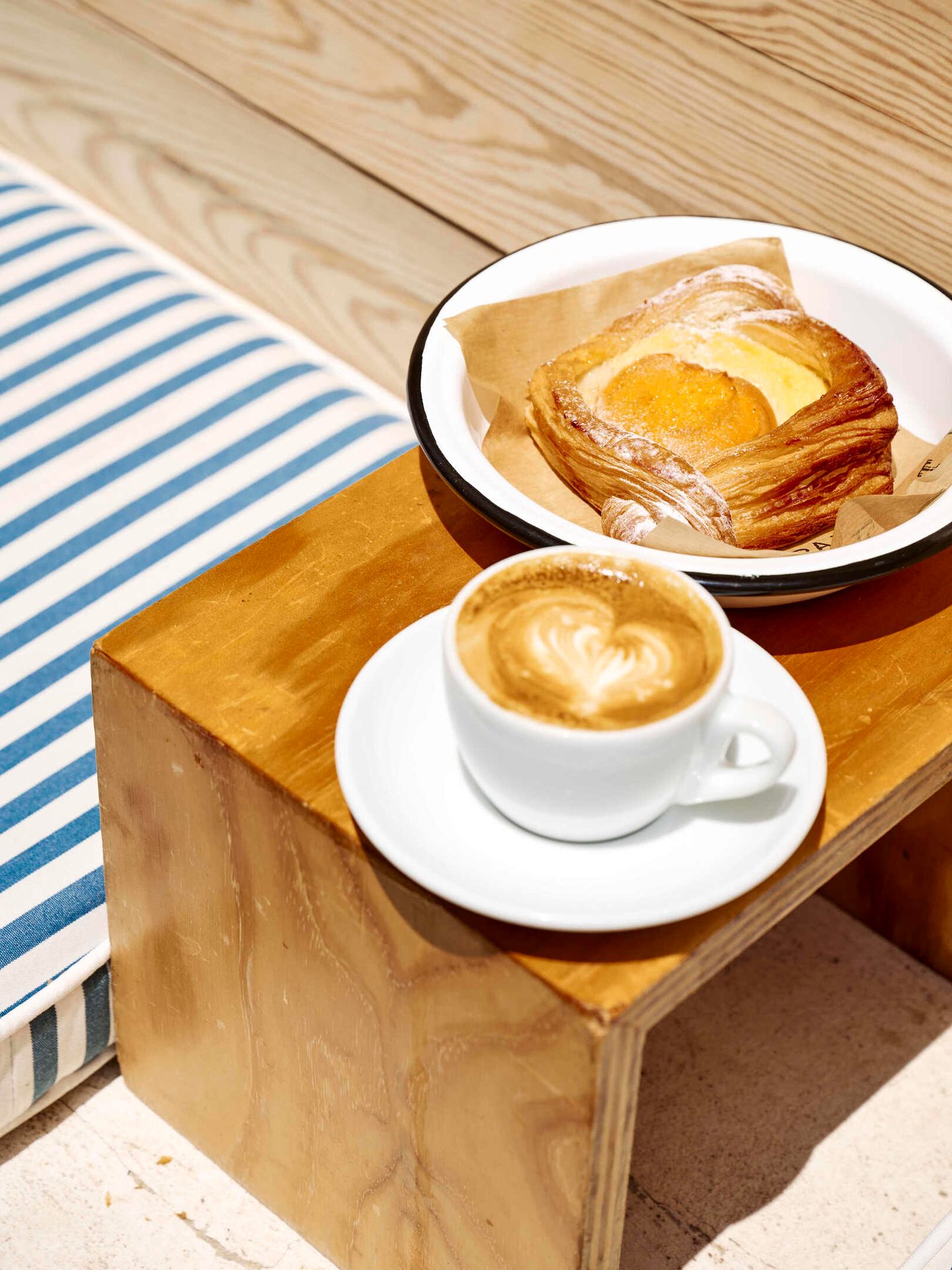 Apricot pastry and latte on a wooden table with a blue striped cushion.