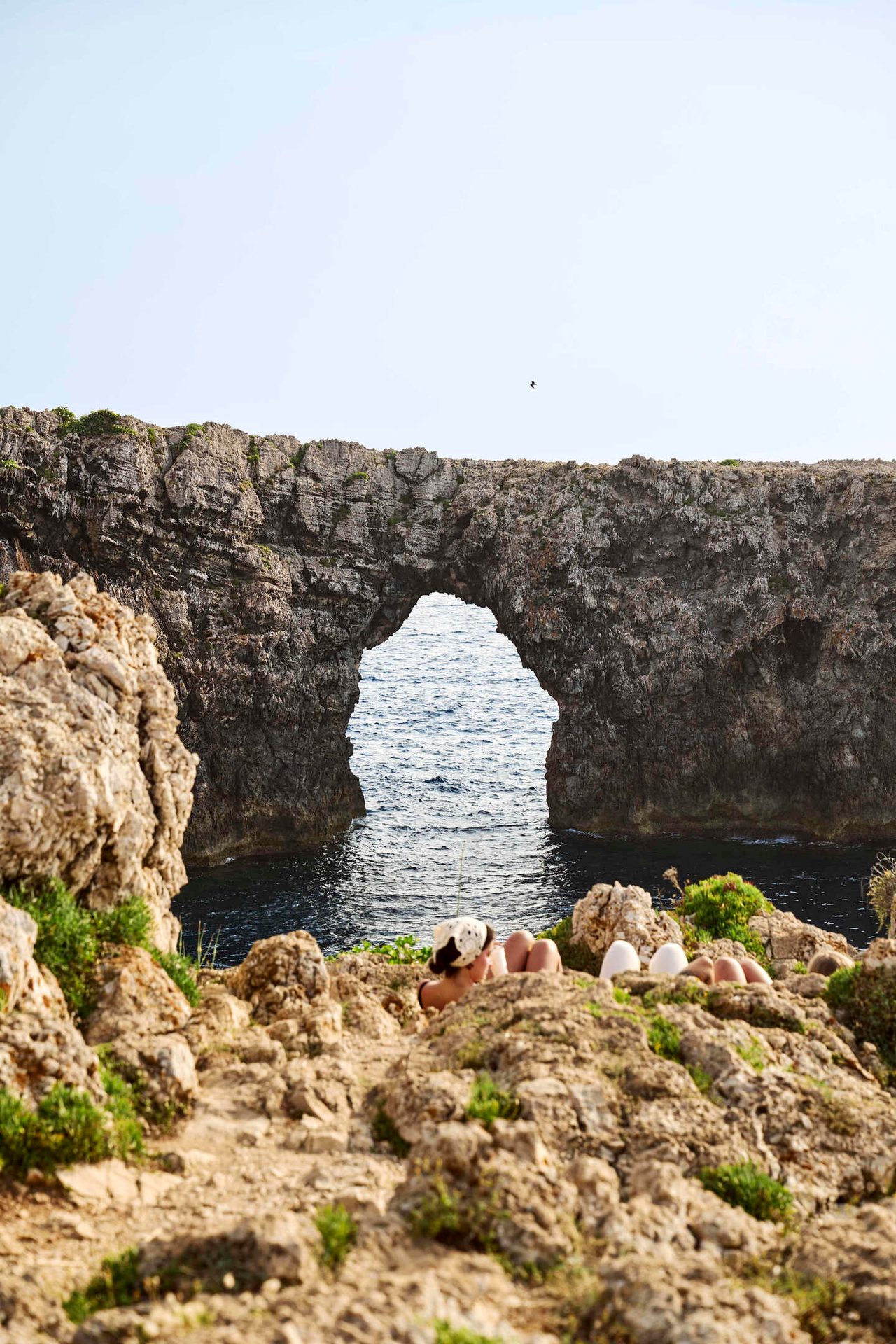 Natural rock arch over the sea with people relaxing on the rocky coast.