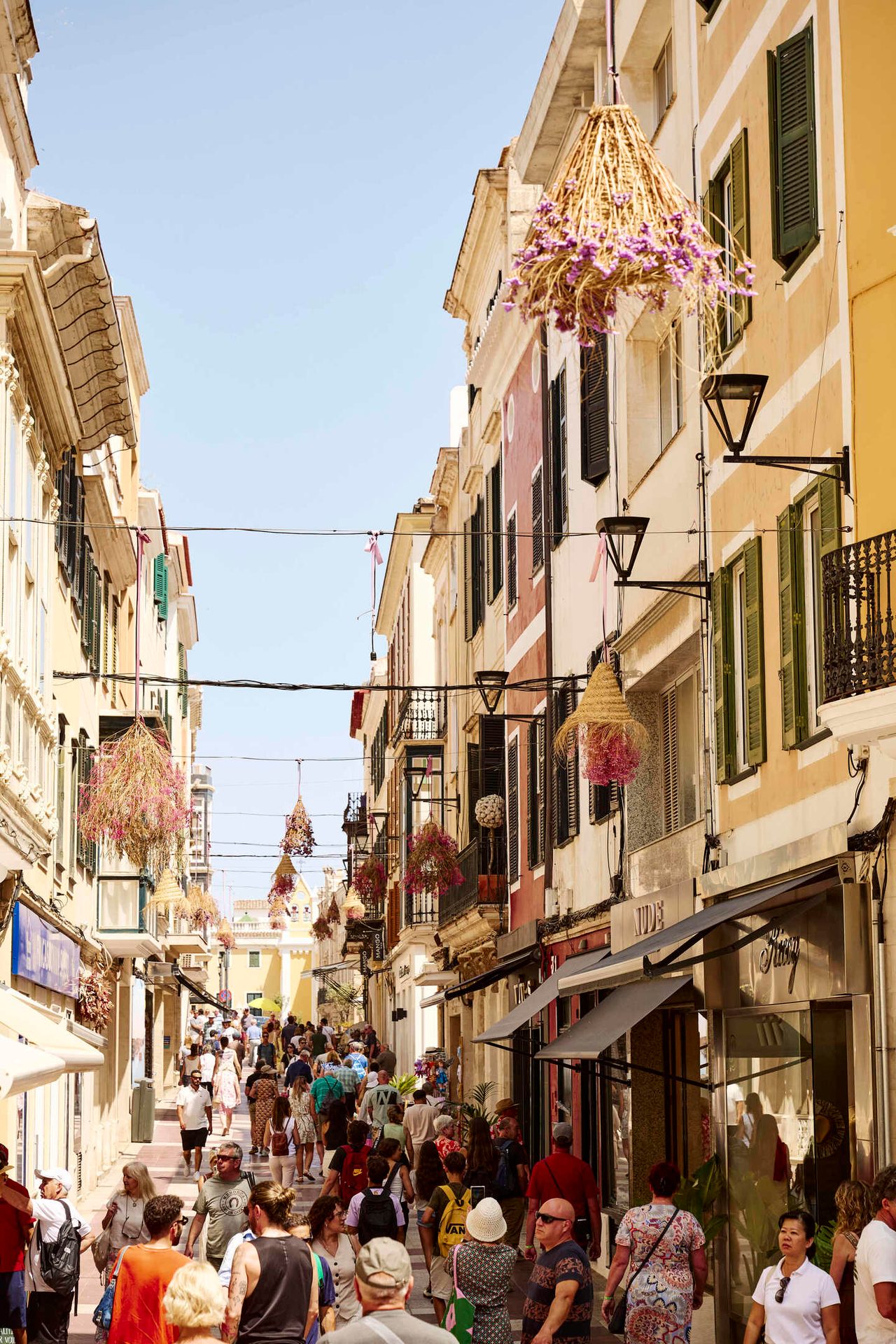 Crowded street lined with old buildings and unique hanging straw & flower decorations.