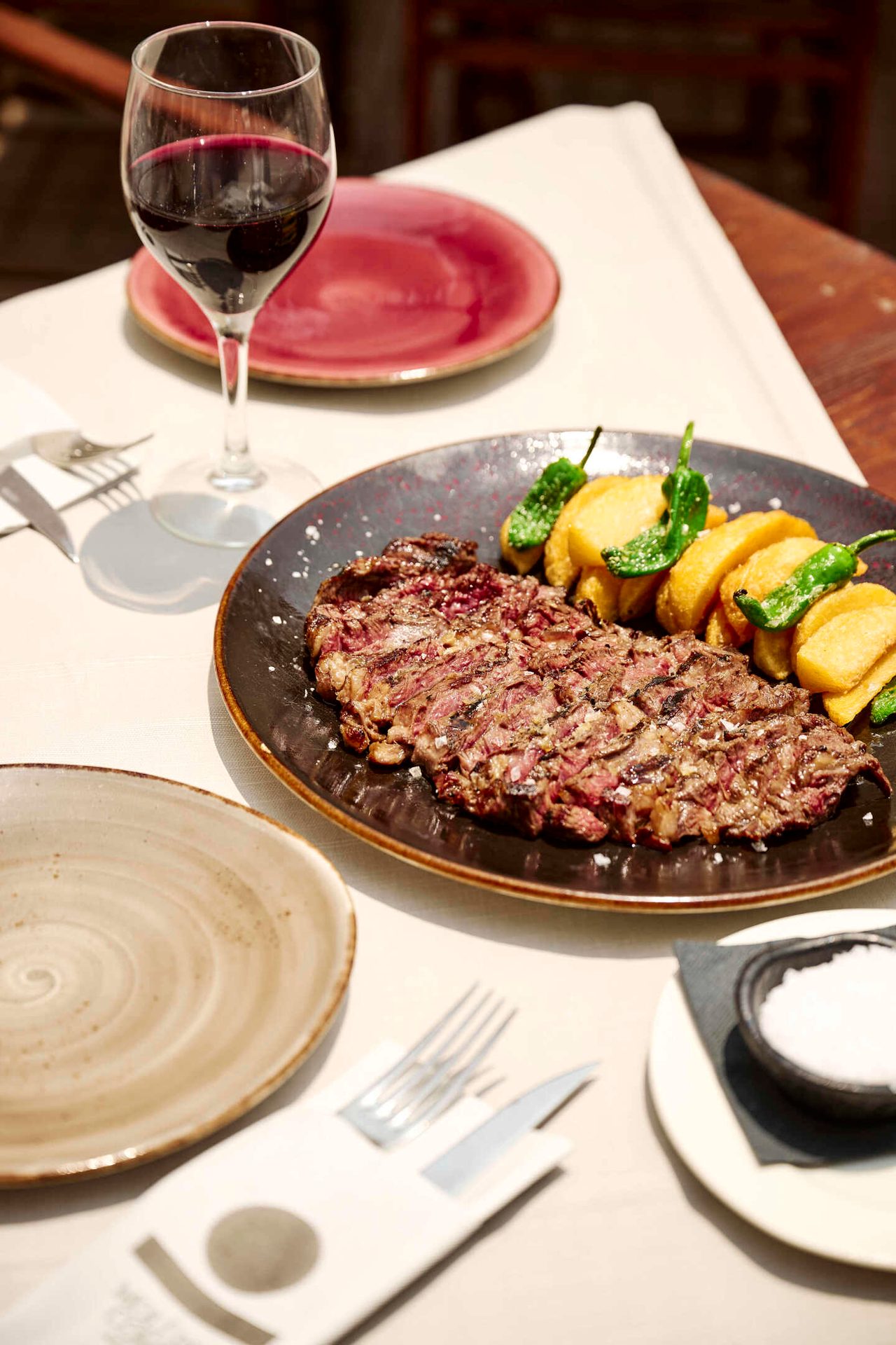 Sliced steak with potatoes, peppers, and red wine.