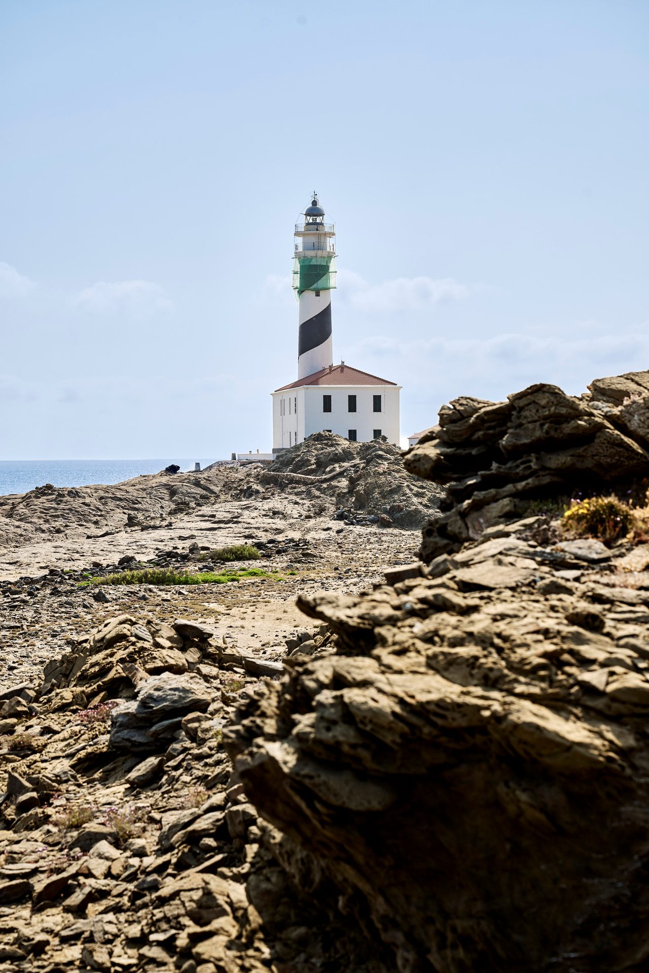 Black and white striped lighthouse on a rocky coast overlooking the sea.