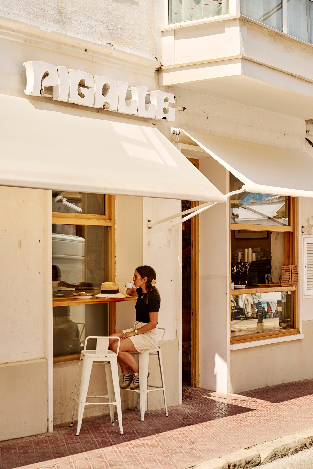 Woman sips coffee outside a cafe named Pigalle on a sunny day.