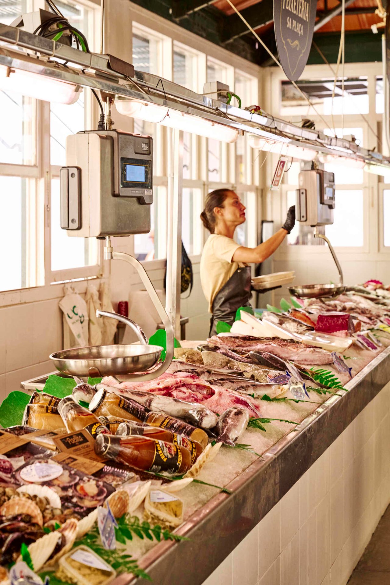 Woman tending a vibrant fish market stall with fresh fish and seafood on ice.