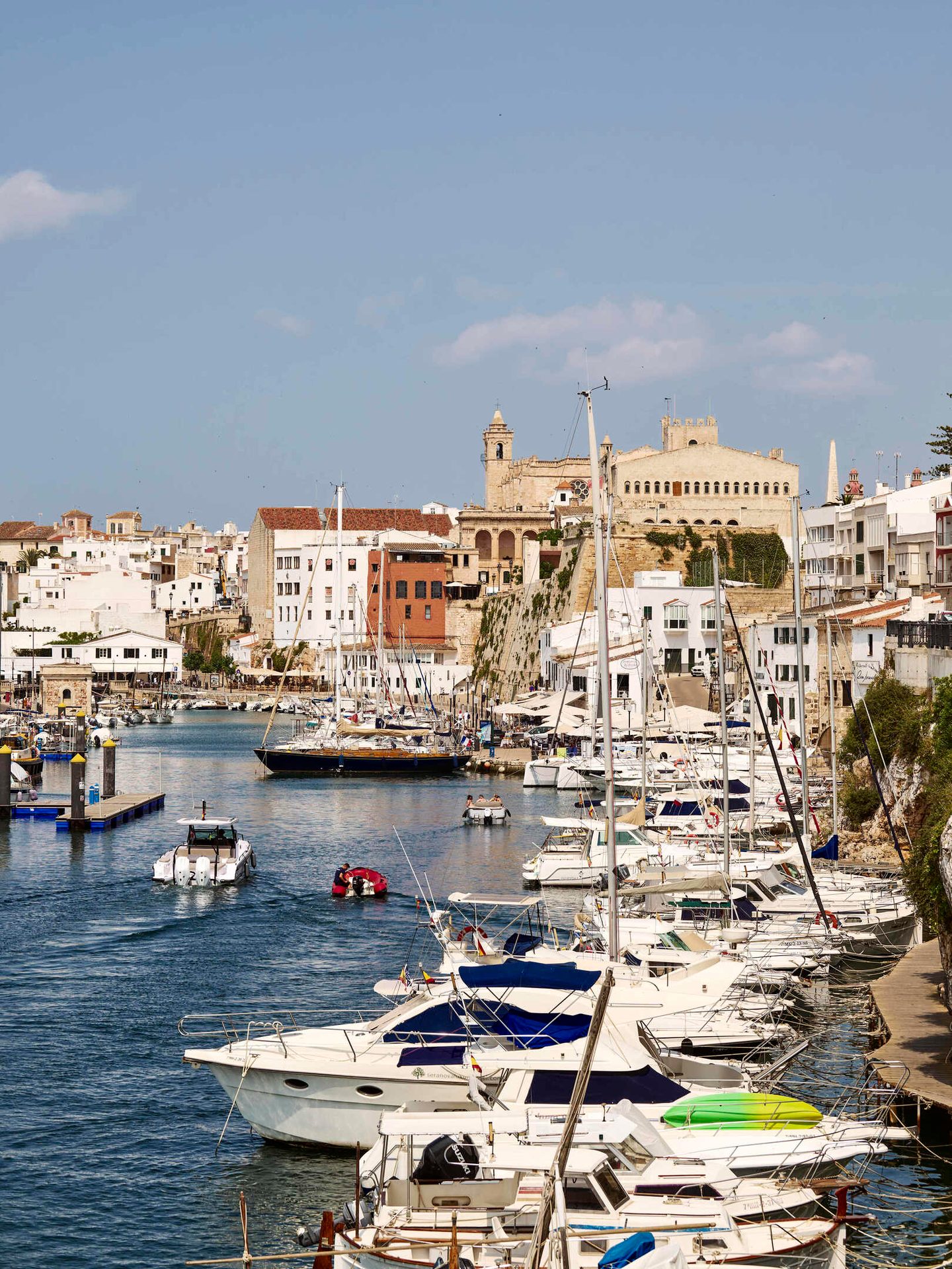 Bustling harbor with boats, a town on cliffs, and blue sky.