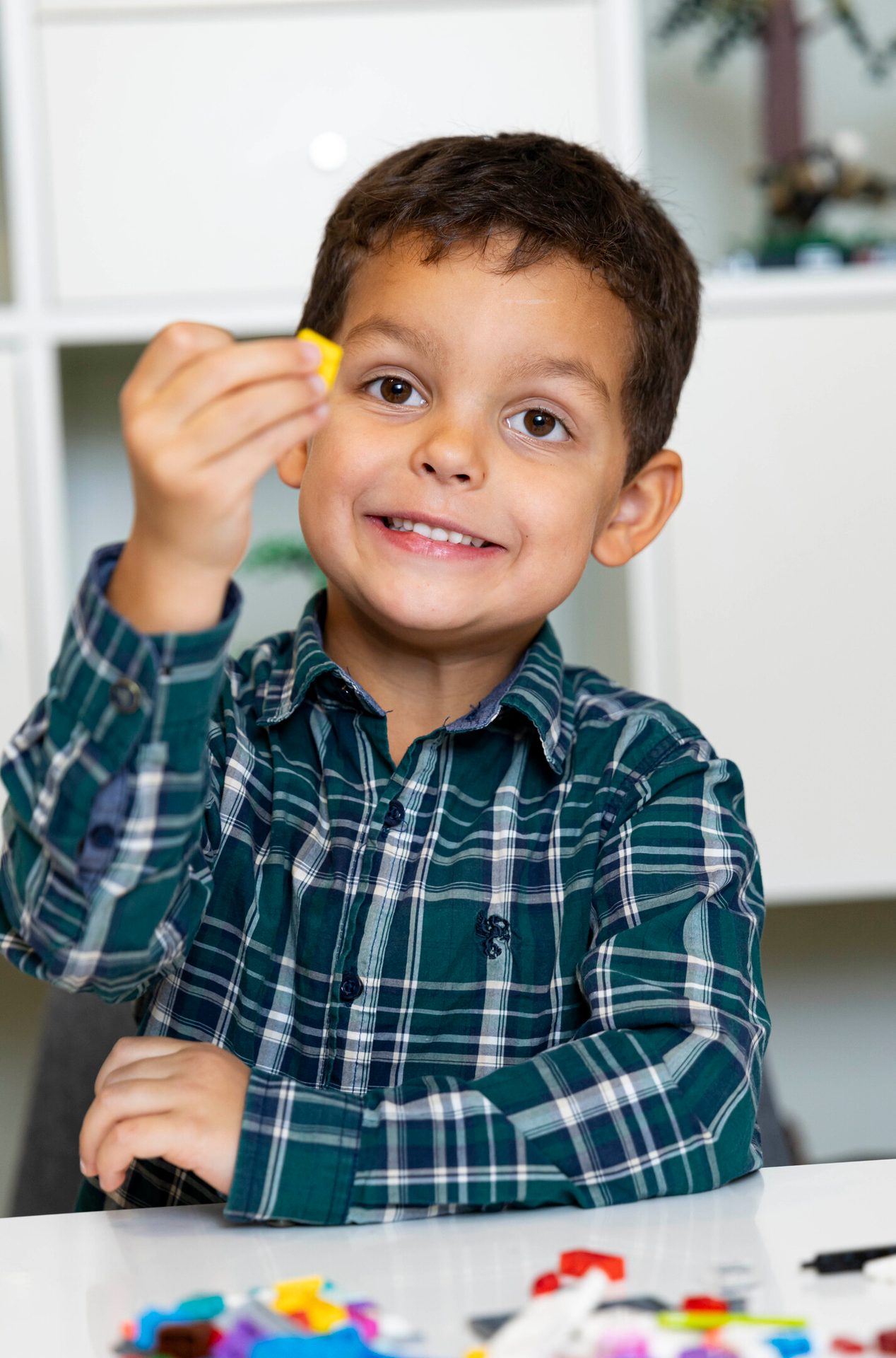 Smiling boy in plaid shirt holding a yellow block.