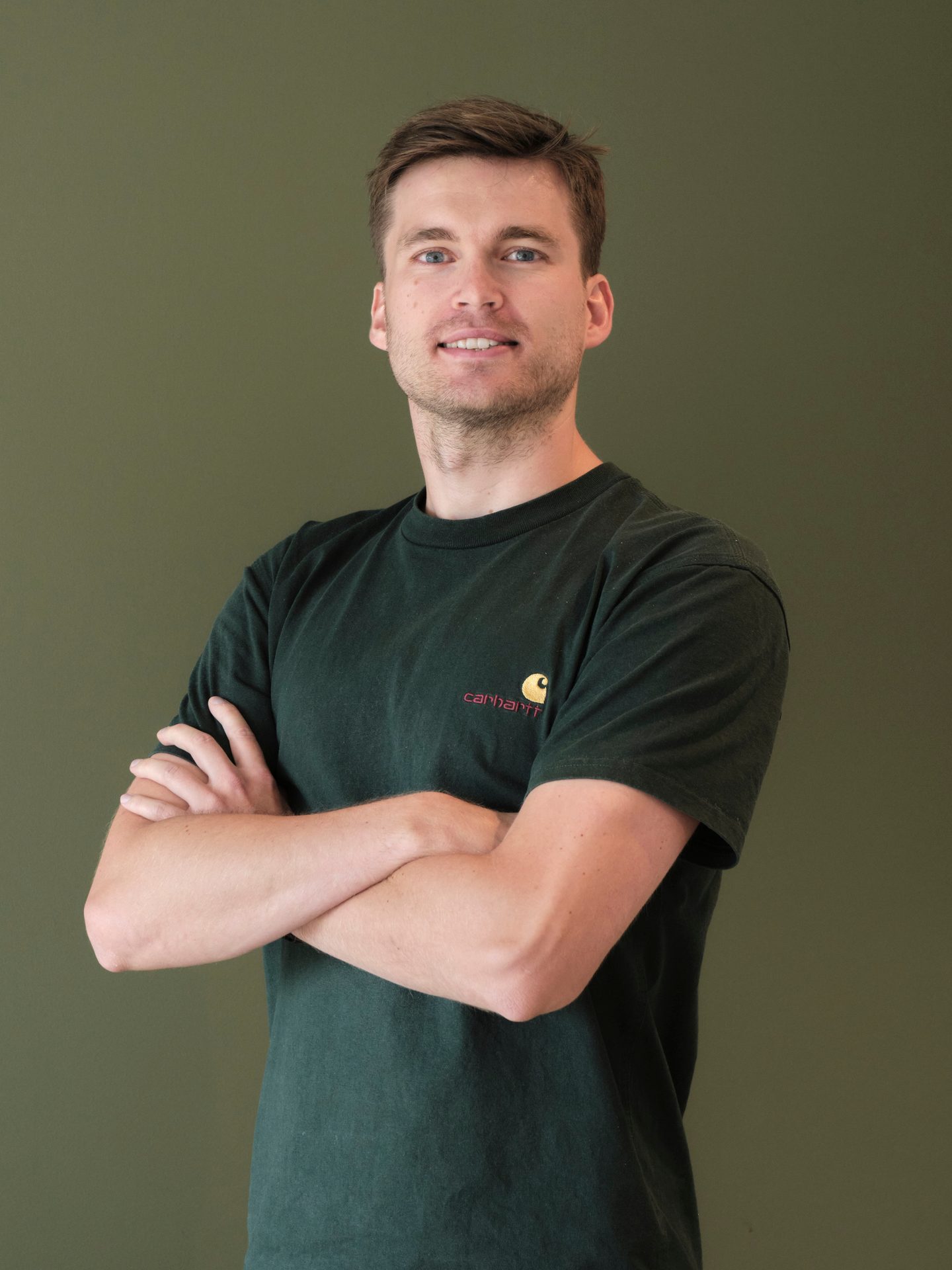 Smiling man in a dark green Carhartt t-shirt with arms crossed.