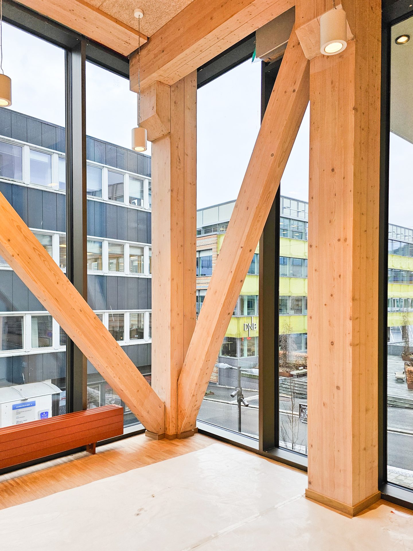 Modern interior with prominent wooden beams, large windows, and a view of city buildings.