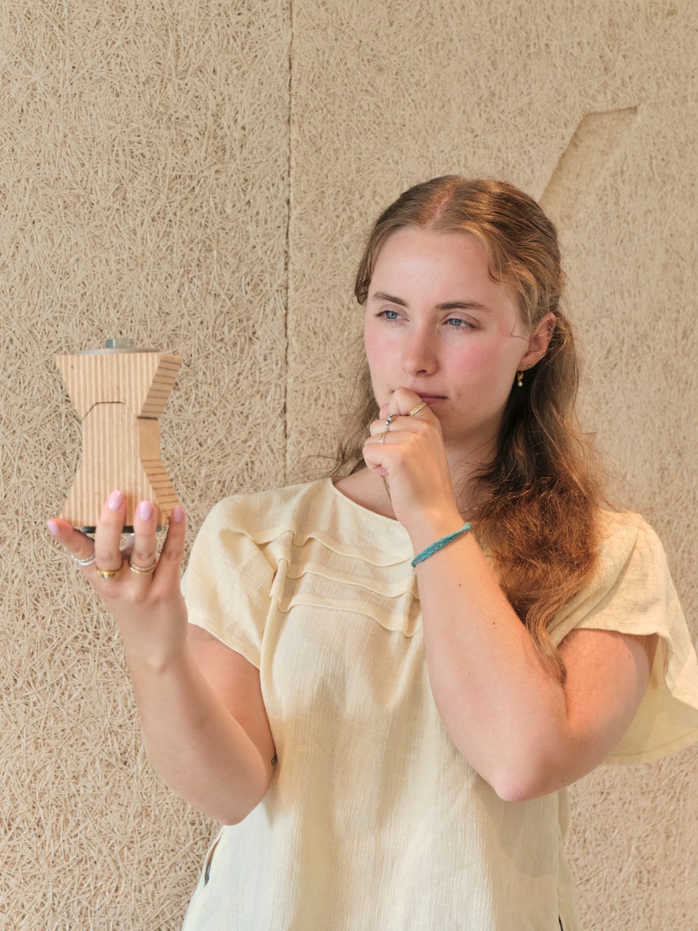 Young woman thoughtfully examining a cardboard Moka pot model.