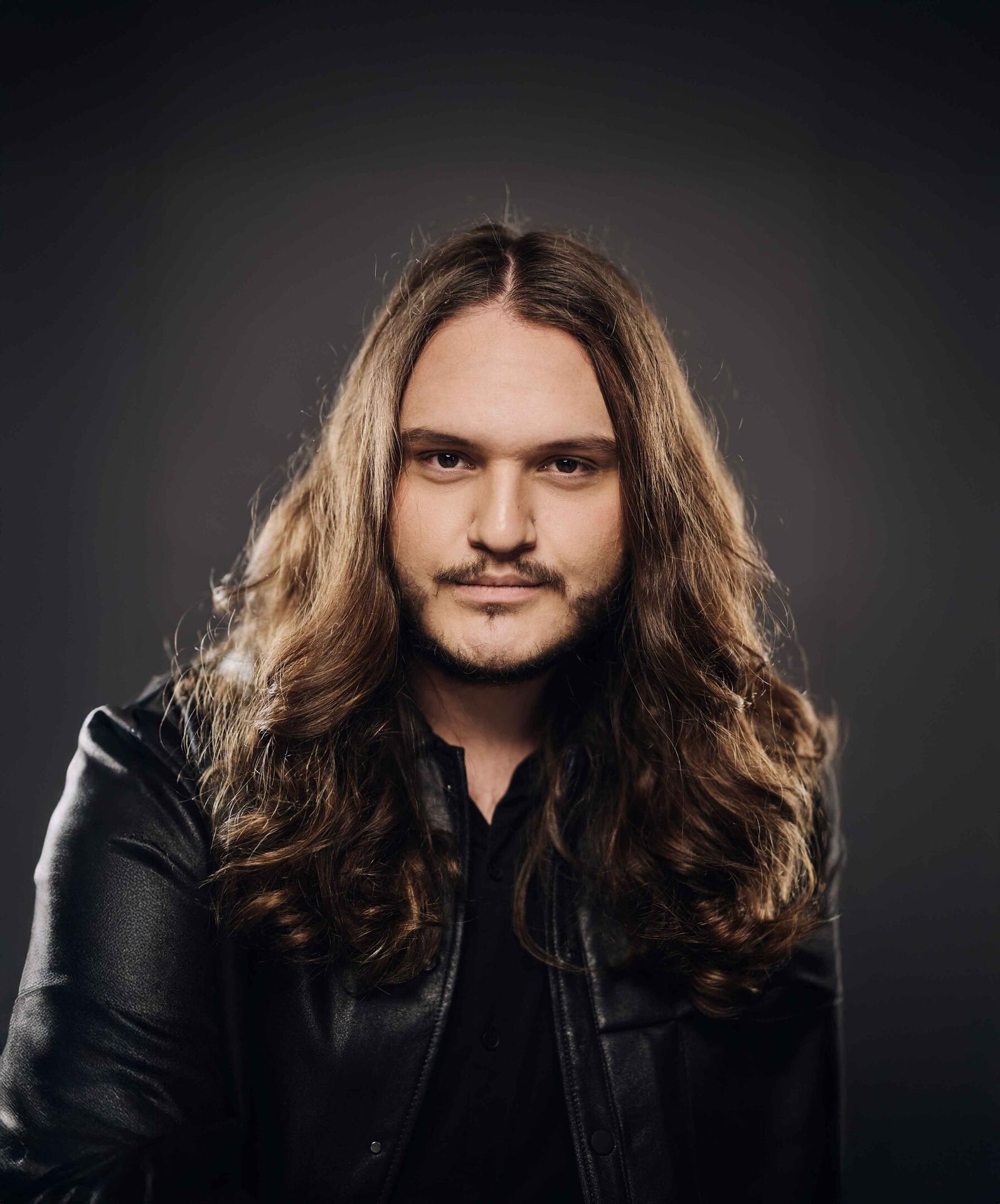 Man with long brown hair and beard in a black leather jacket.